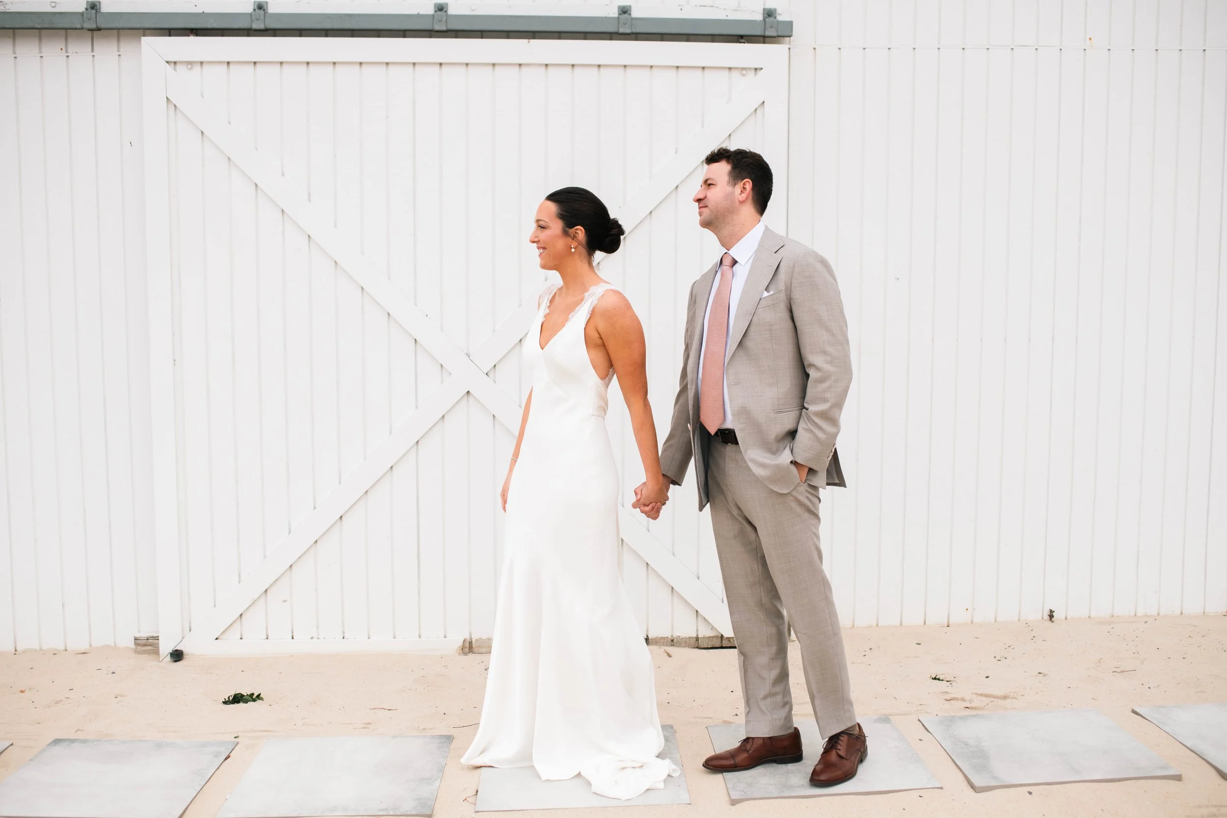 A candid, editorial shot of a bride and groom walking hand-in-hand along the sand during their East Hampton beach wedding.