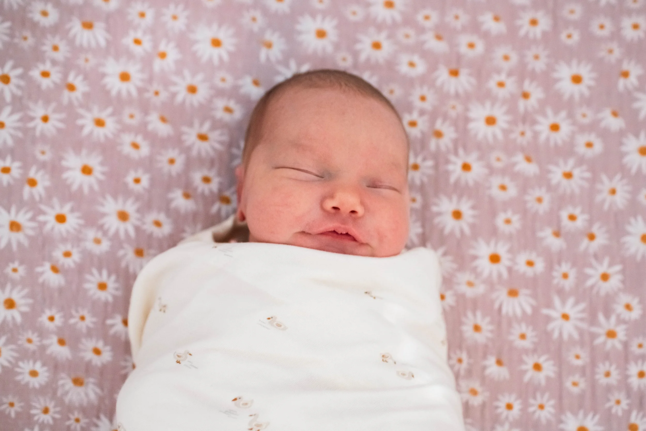 A high-angle lifestyle shot of a young girl sleeping soundly in a wooden crib within a brightly lit, decorated nursery, capturing a quiet moment of childhood rest.