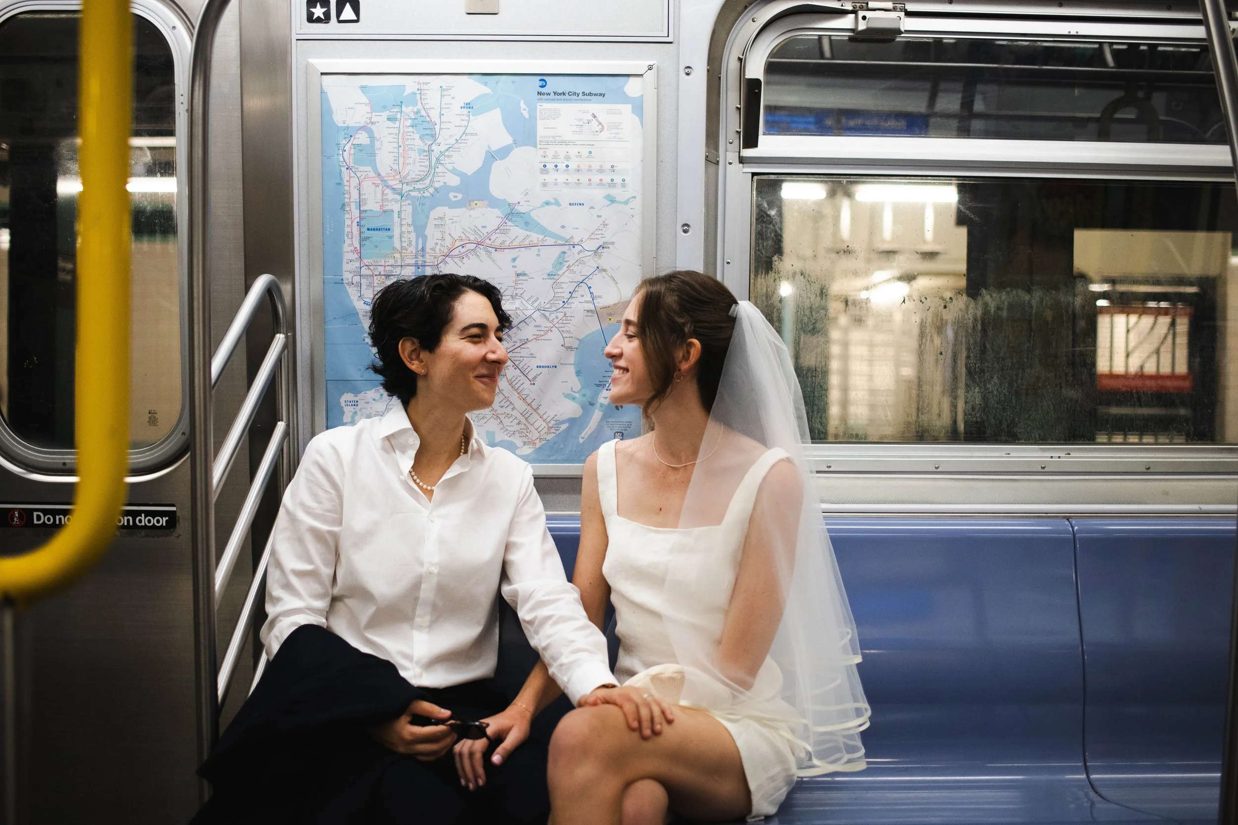 Queer couple smiling together on the subway on their way to their NYC courthouse wedding