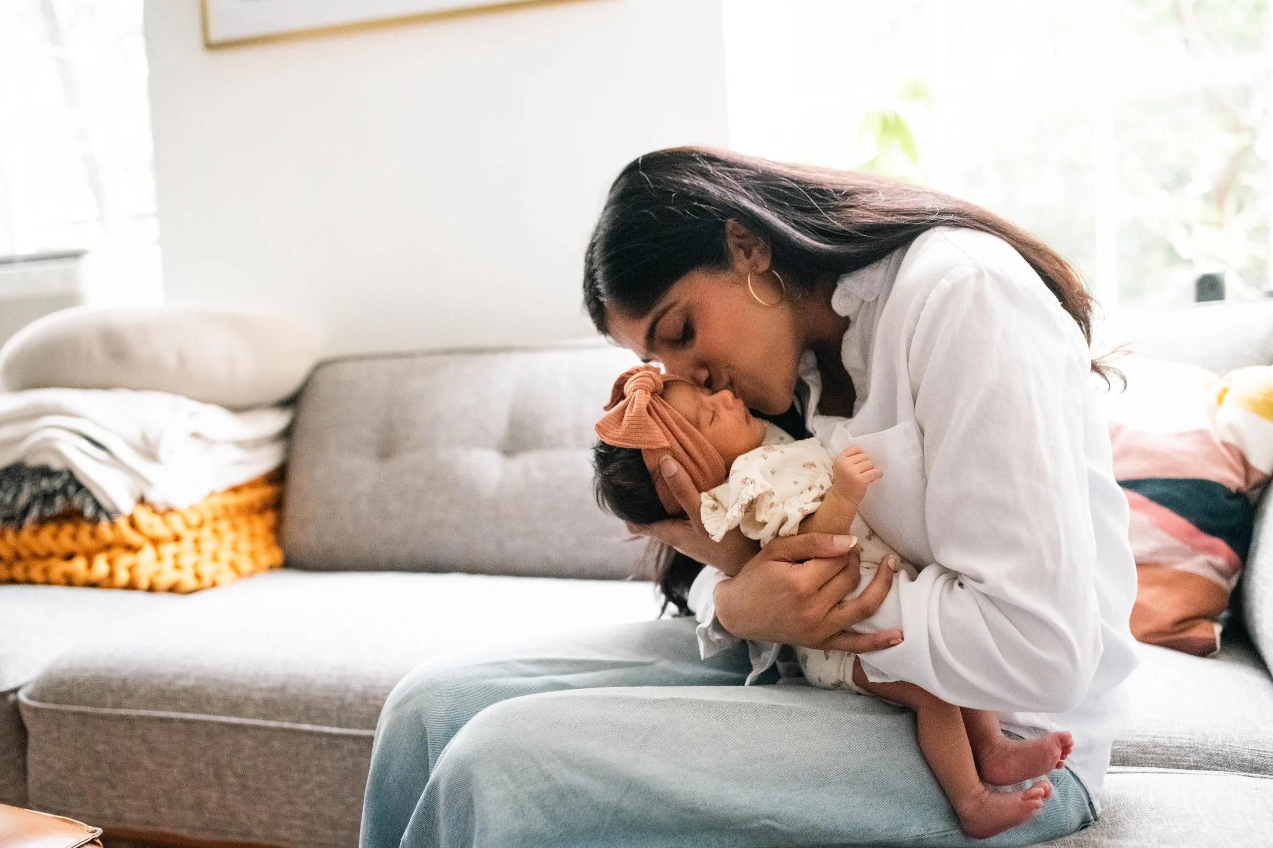 New mom sits on her couch in NYC apartment with newborn.