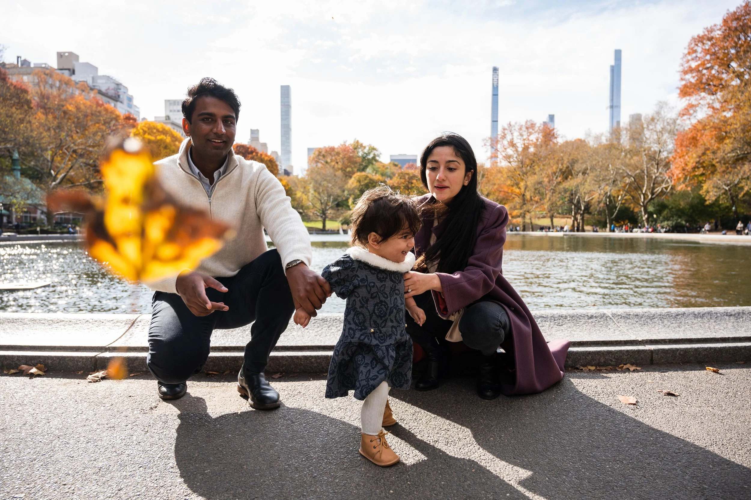 Mother, father, and daughter laughing together near the boat pond in Central Park NYC