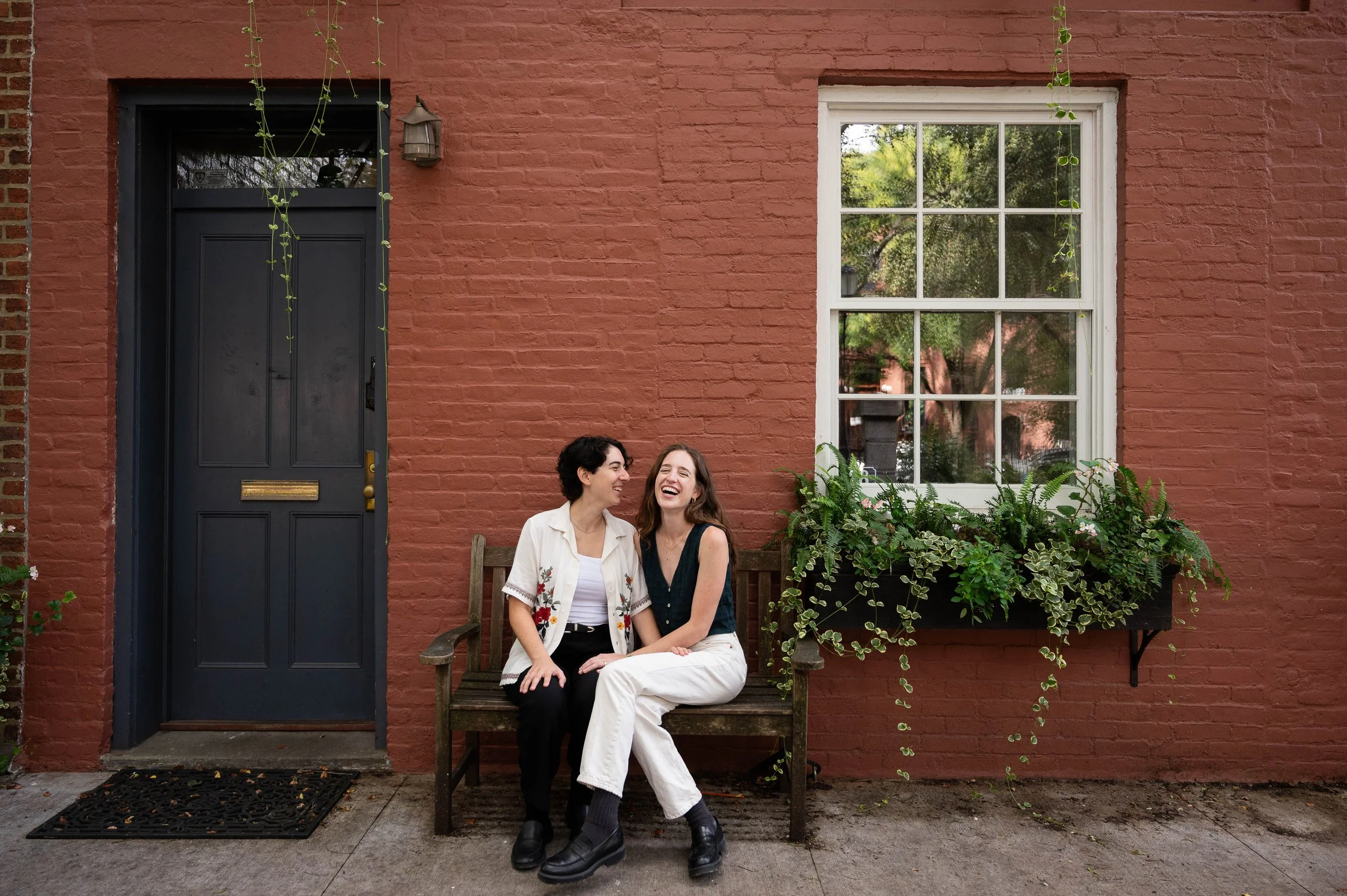Couple sitting on a bench laughing together in Cobble Hill Park during their Brooklyn engagement photoshoot