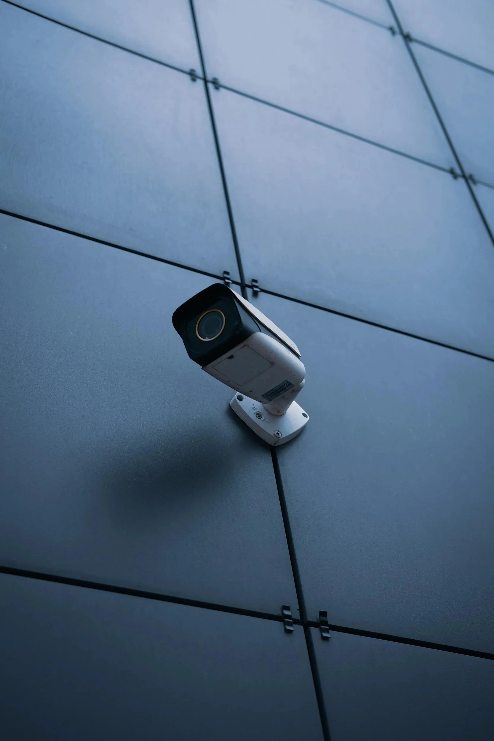 Close-up of a security camera mounted on a modern building's exterior wall with large, flat gray panels.