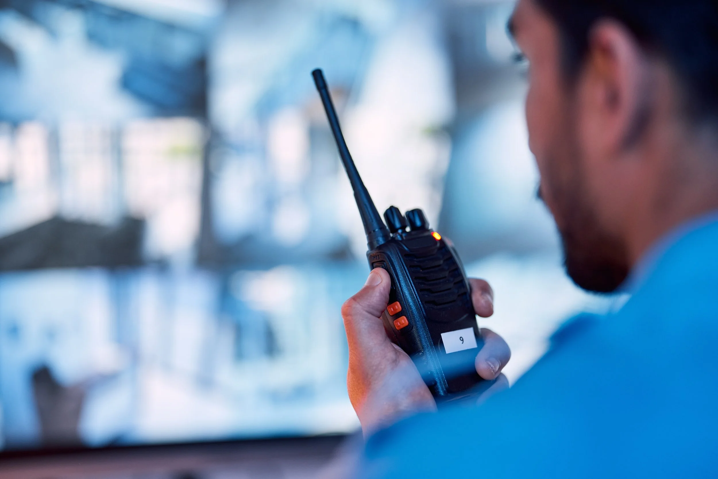Man holding a walkie-talkie with an antenna, indoors, blurred background