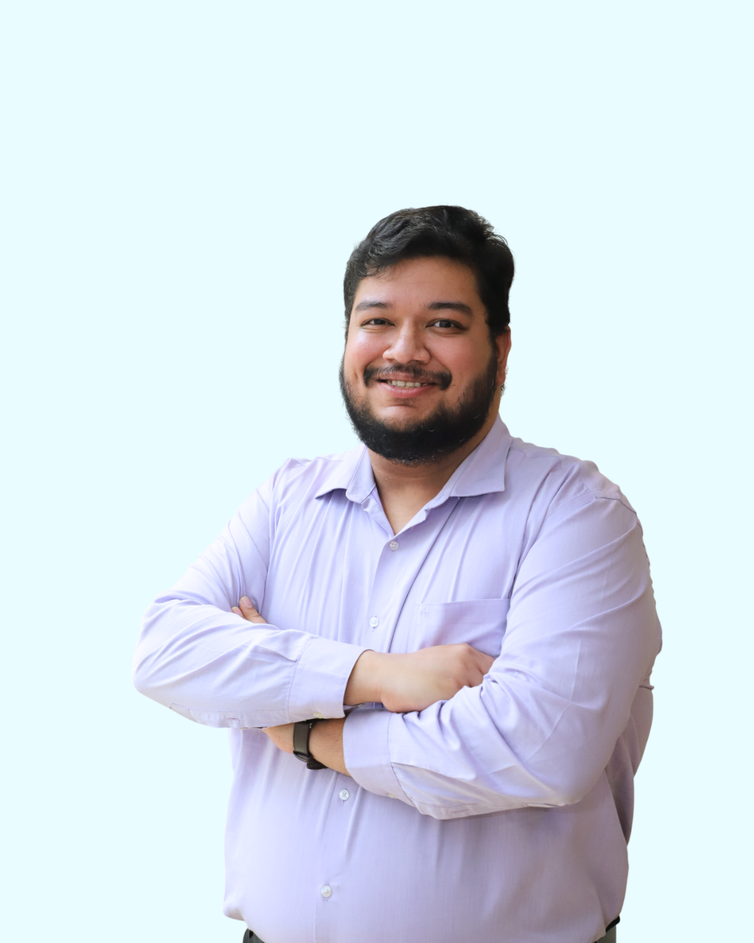 Portrait of a smiling man with dark hair and beard wearing a light purple button-down shirt, arms crossed, against a light blue background.