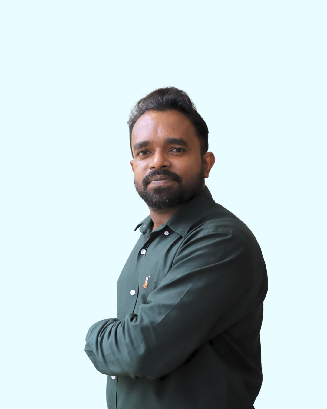 A man with a beard and dark hair, wearing a dark green shirt with a small logo, poses with arms crossed against a light blue background.