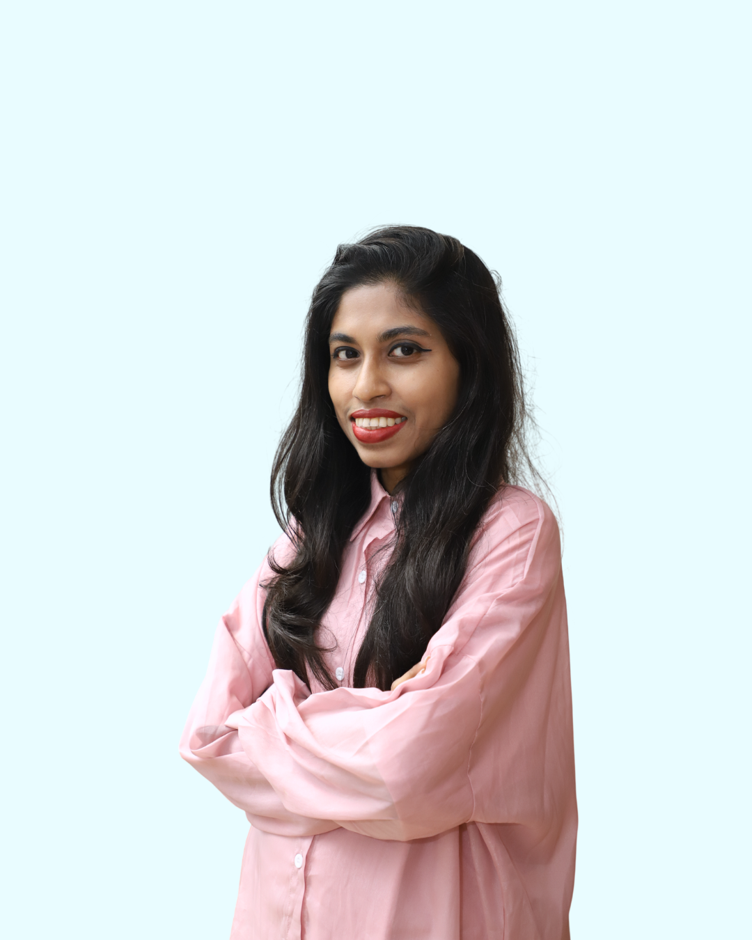 A woman with long dark hair, wearing a pink button-up shirt, smiling with arms crossed, against a light blue background.