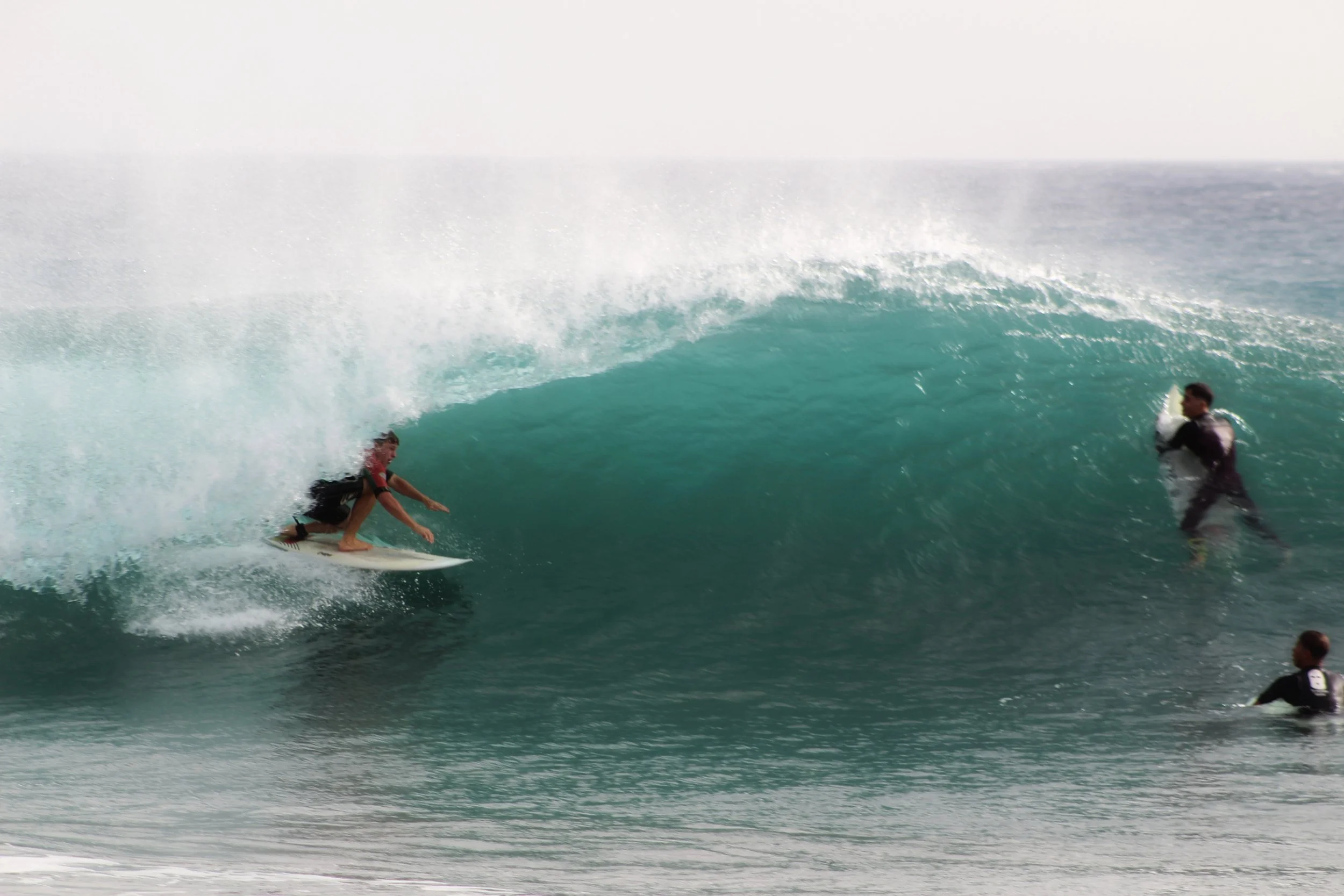 Una persona surfeando una ola en el mar, con dos rescatistas en el agua observándolo.