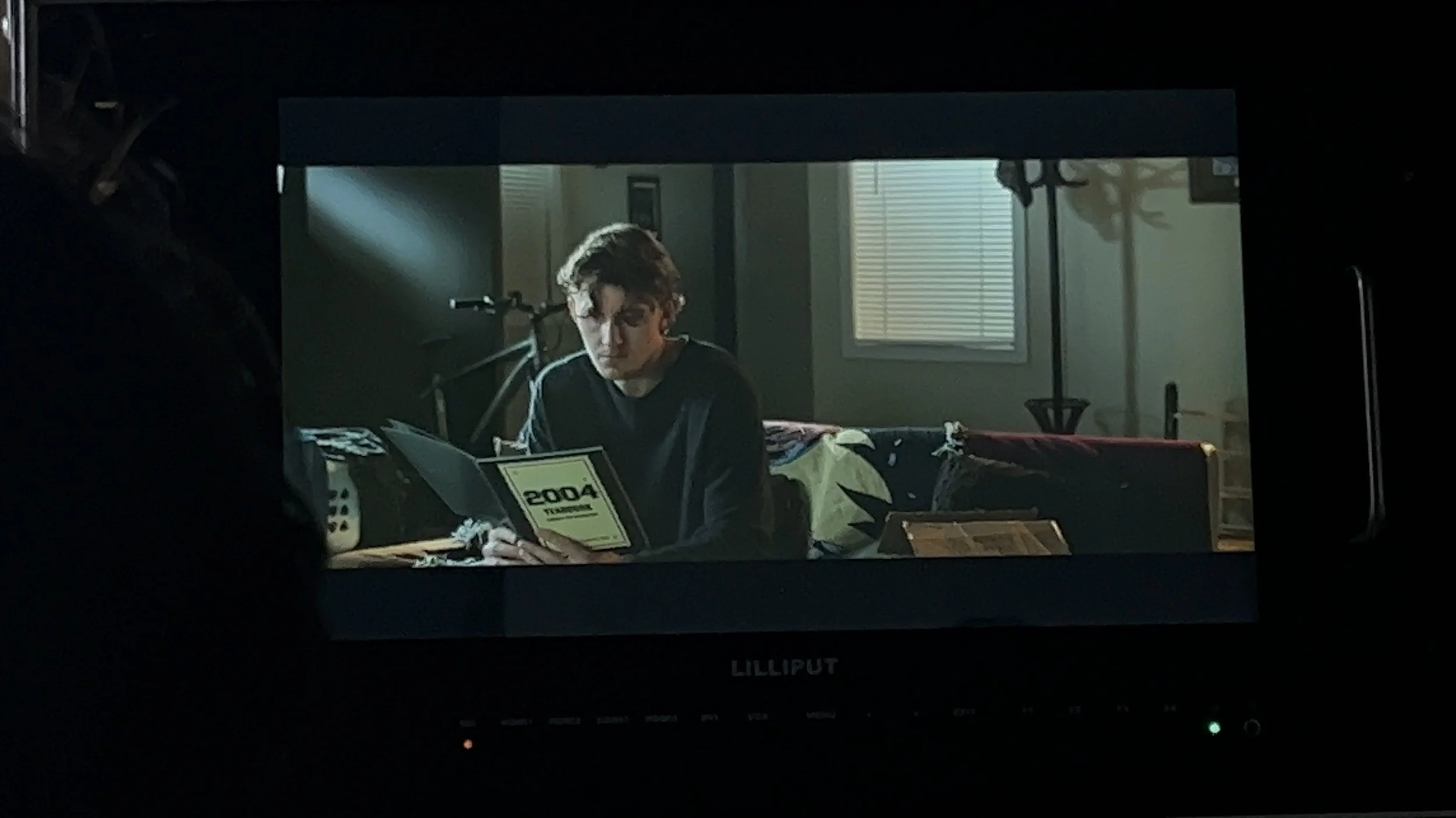 A young man with curly hair looking at a notebook in a dimly lit room, with a bicycle in the background and sunlight coming through a window.