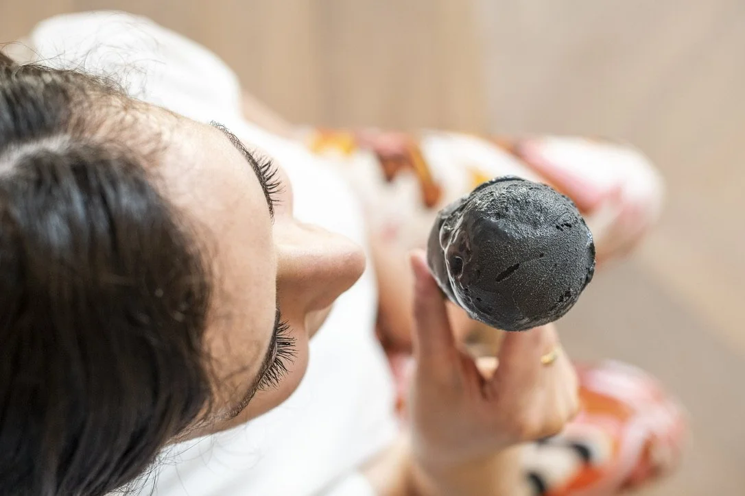 A woman with dark hair and long eyelashes is holding a black ice cream artwork by Joao Loureiro close to her face.
