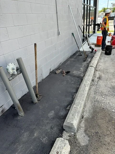 Workers renovating sidewalk outside a building, with tools and construction materials on site.