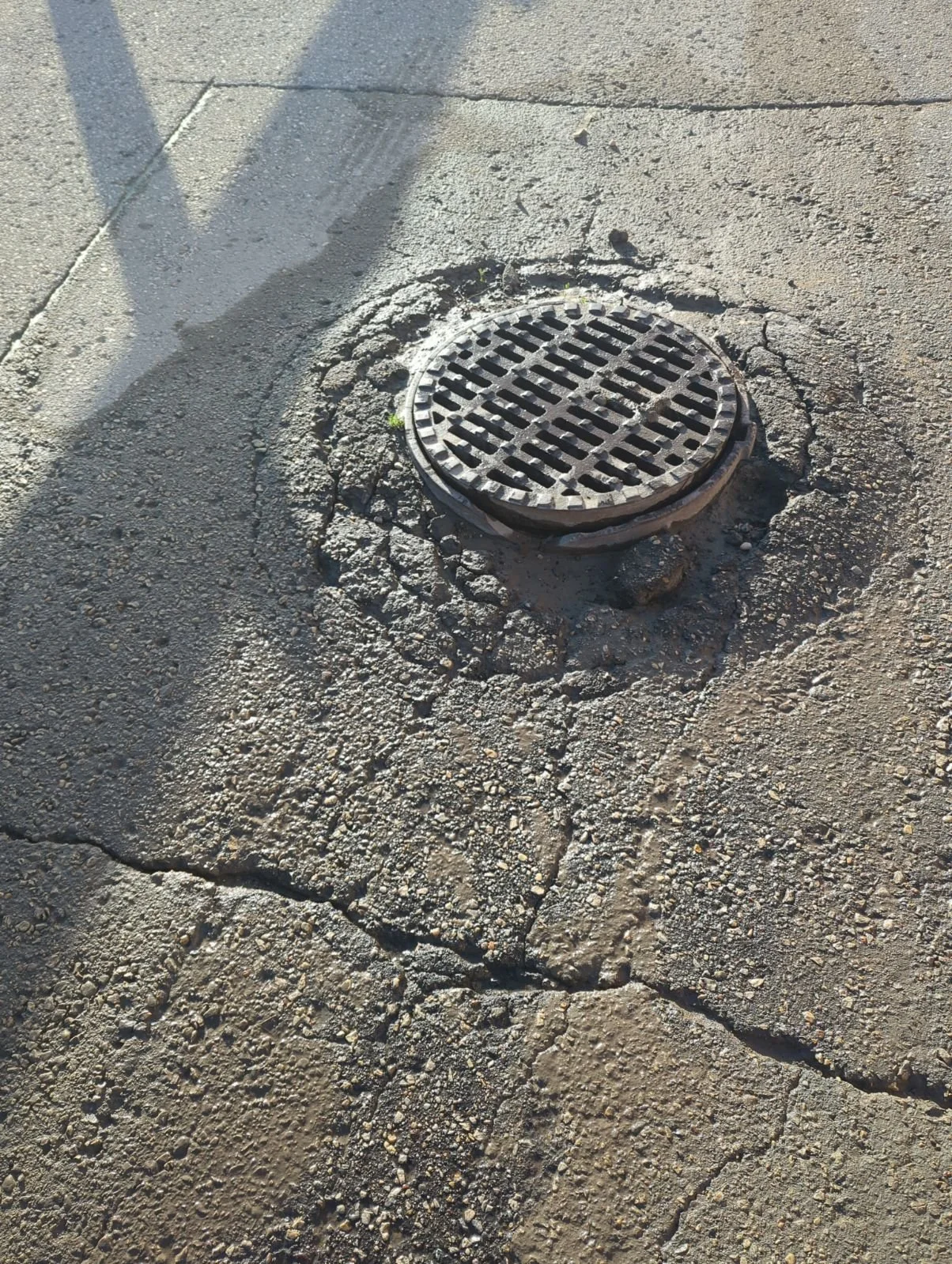 A round metal storm drain cover on a cracked asphalt sidewalk.