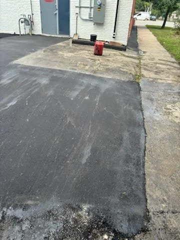 Newly paved asphalt driveway with a red gas can on top and construction tools nearby.