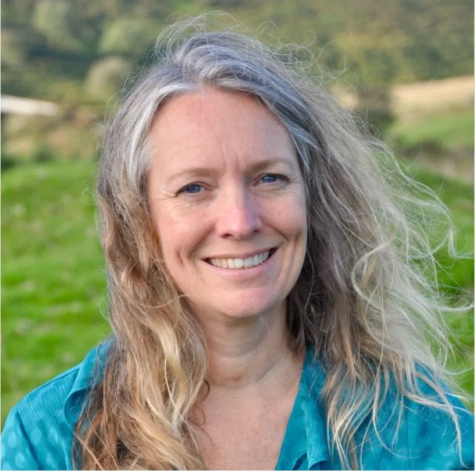 Laura Walker, Burnout Coach and dementia specialist, smiling outdoors with a blurred green landscape background.