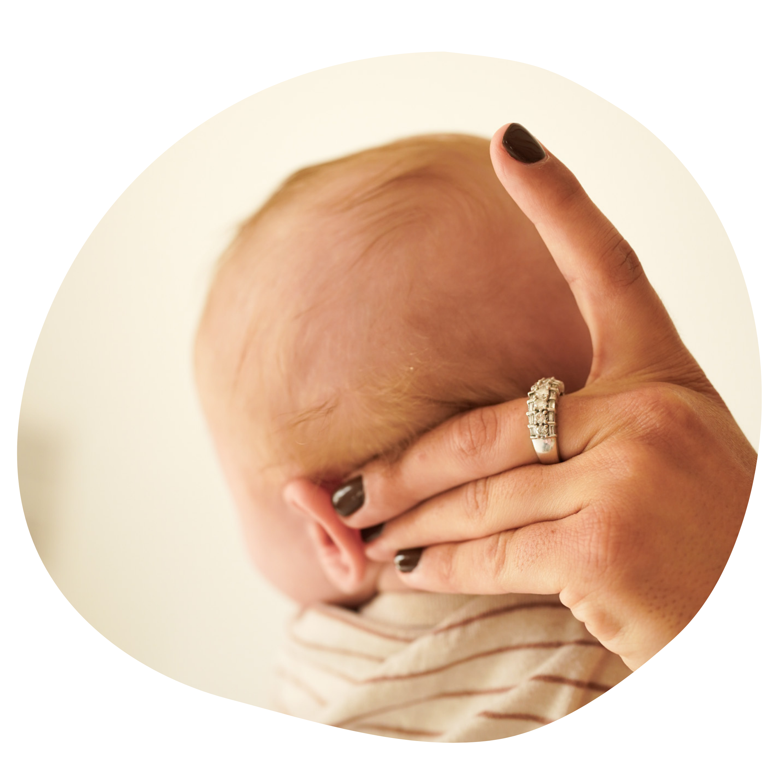 A person with dark nail polish holds a baby's head with one hand, wearing a ring with multiple diamonds.