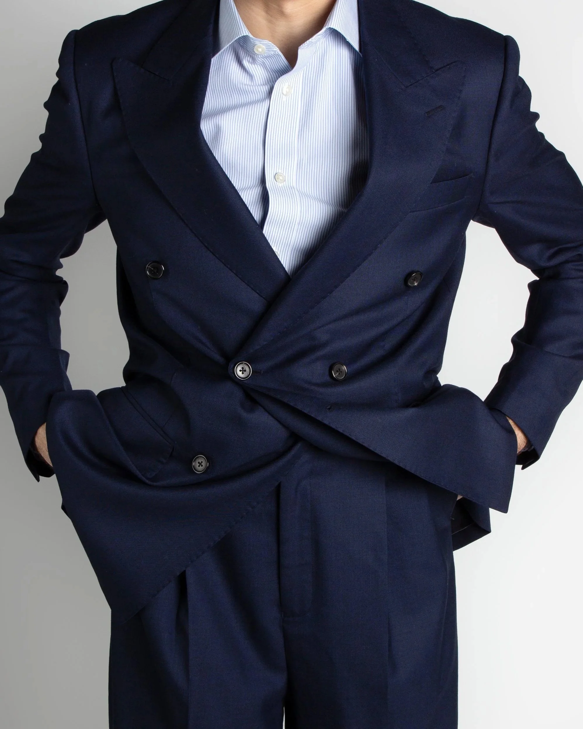 Close-up of a person wearing a navy blue double-breasted suit and a white button-up shirt with light blue vertical stripes.
