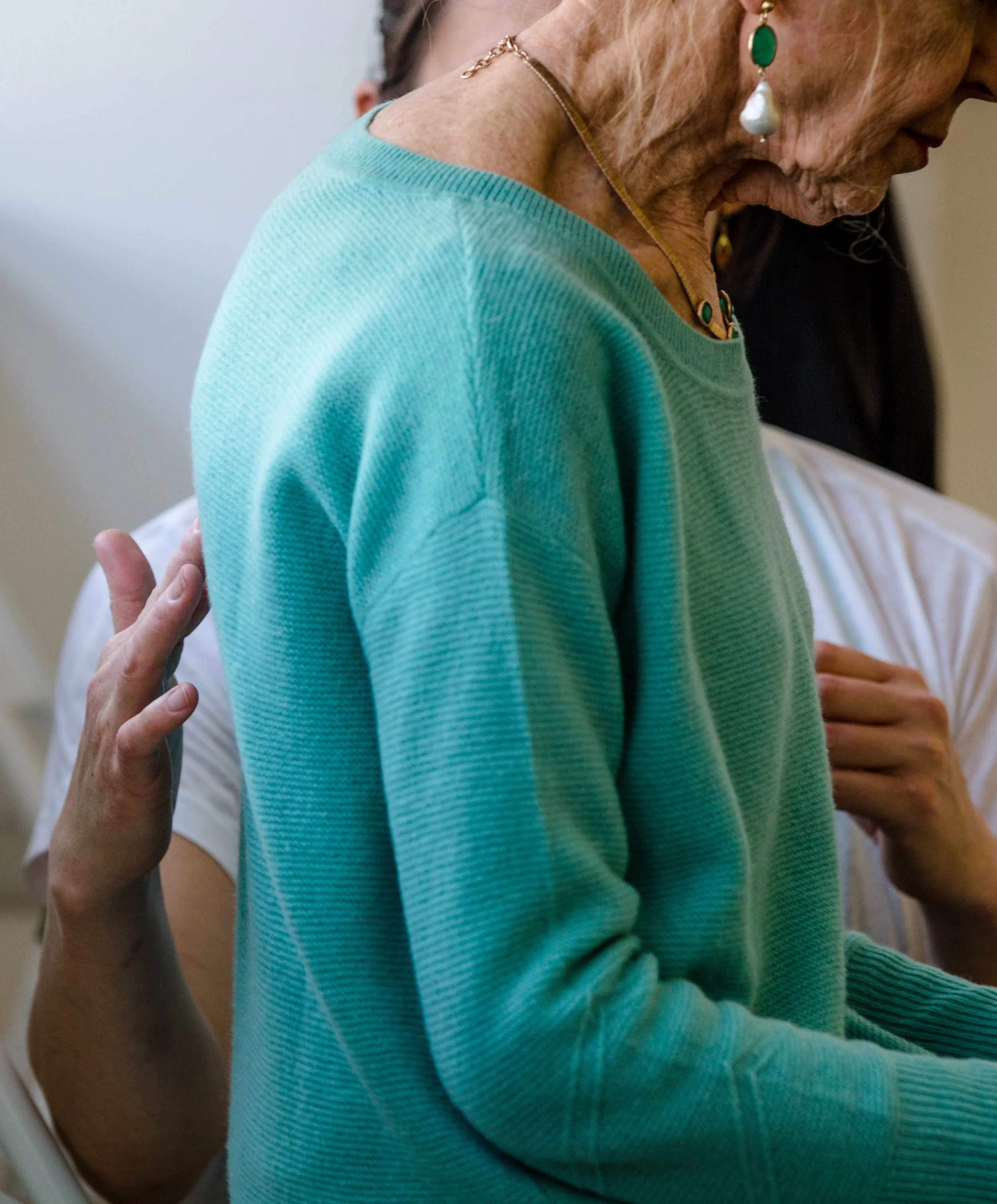 Close-up of an elderly woman receiving a massage or therapy treatment, with a person in white clothing behind her giving hands-on support.