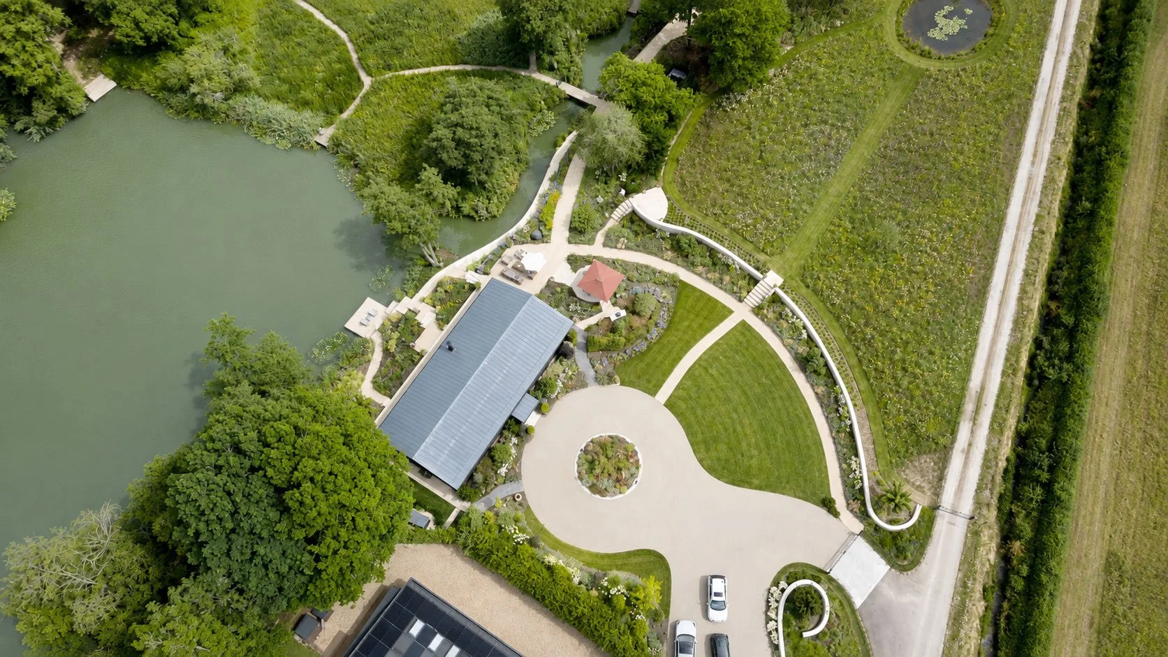 Aerial view of The Lake House showing the relationship between the house, lake, curved garden structure and wildflower meadow.