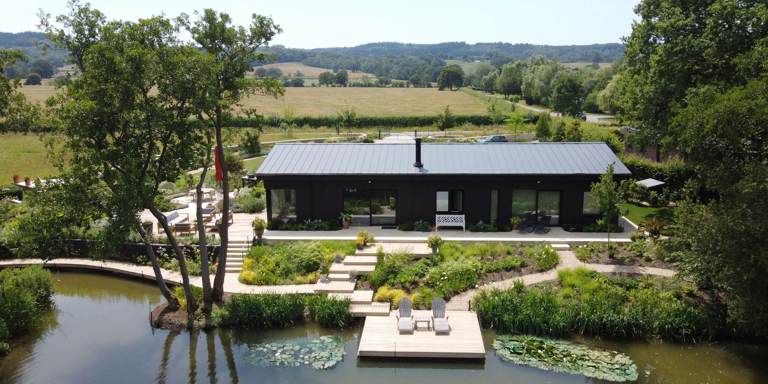 Water’s Edge lake house and contemporary garden viewed across the lake, with naturalistic planting and landscape design by Doug Holloway Landscape Design.
