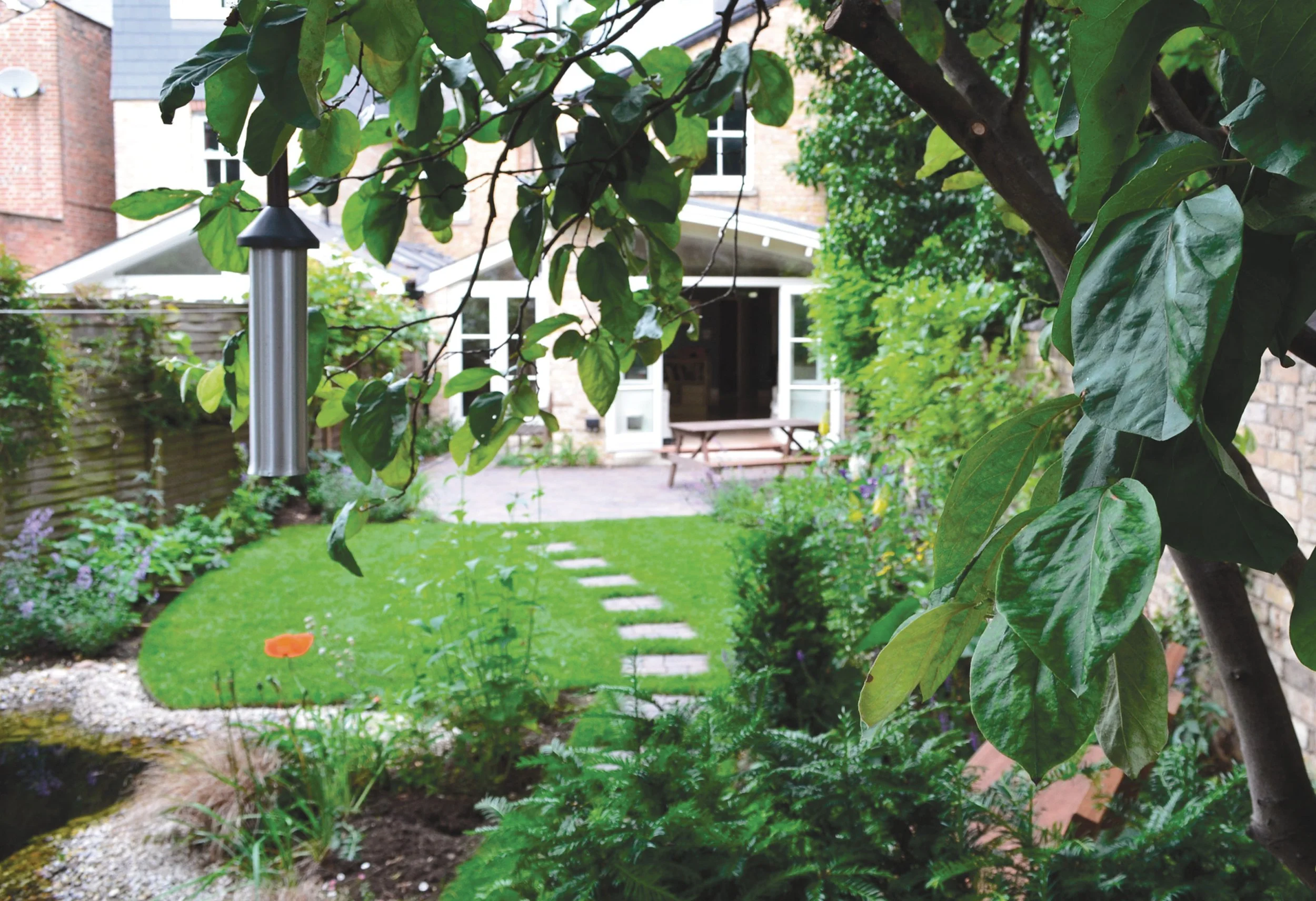 Compact garden with stepping-stone lawn, water feature and lush planting beneath mature trees.