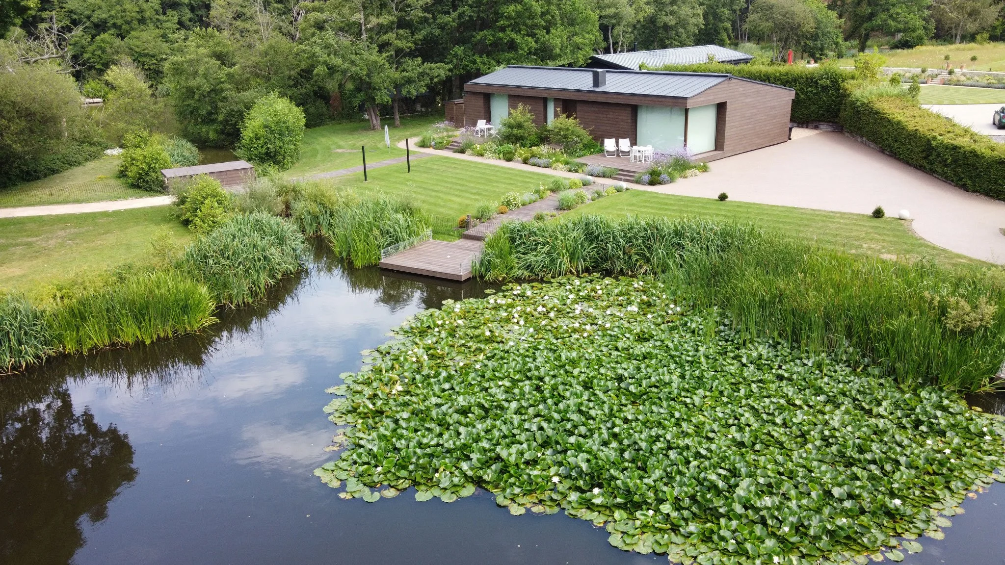 Aerial view of The Fishing Lodge in Surrey, showing the converted barn, fishing lake, waterside planting and timber fishing swims.