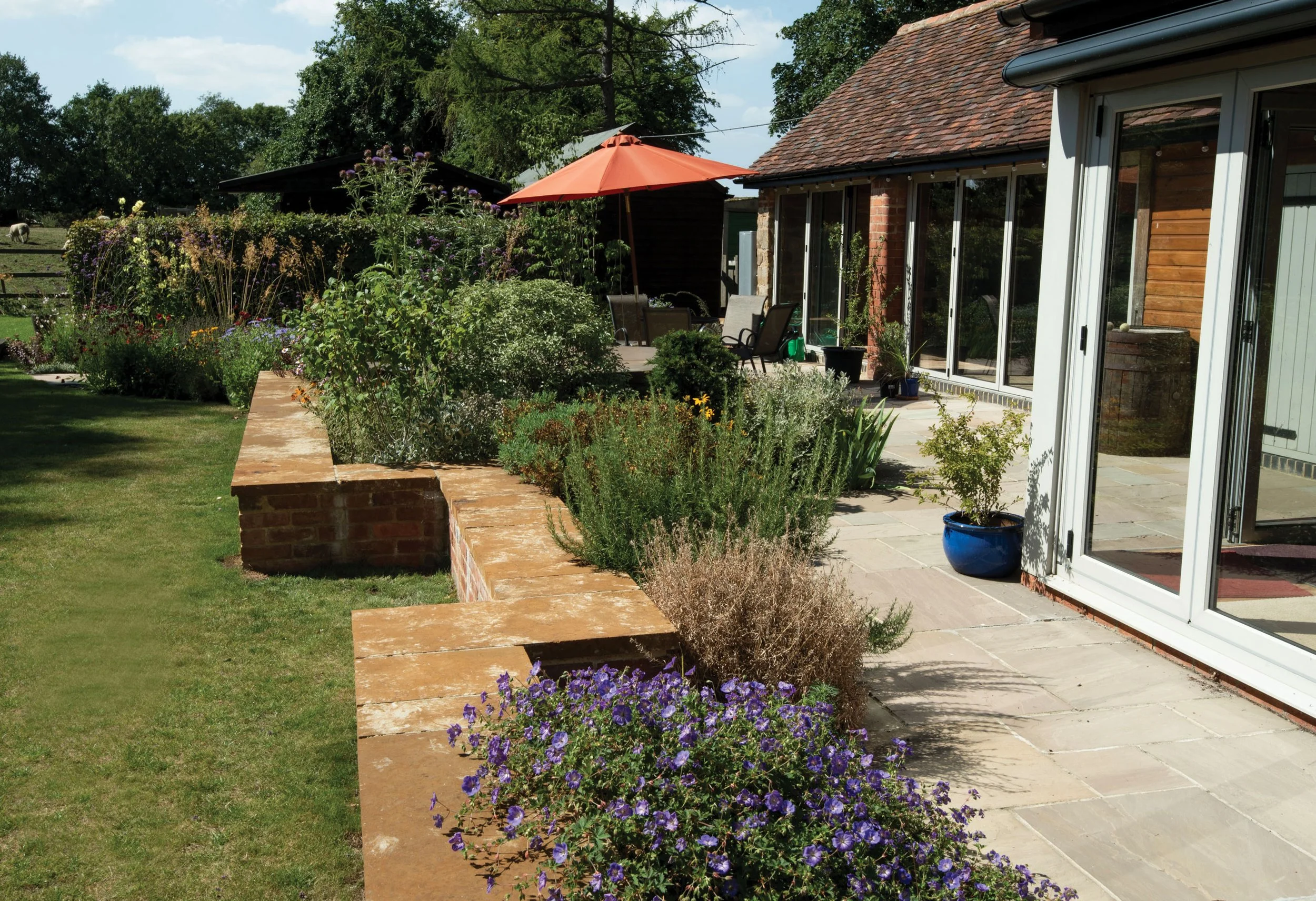 Courtyard seating space with low brick walls, perennial planting and the converted barn forming an intimate outdoor room.
