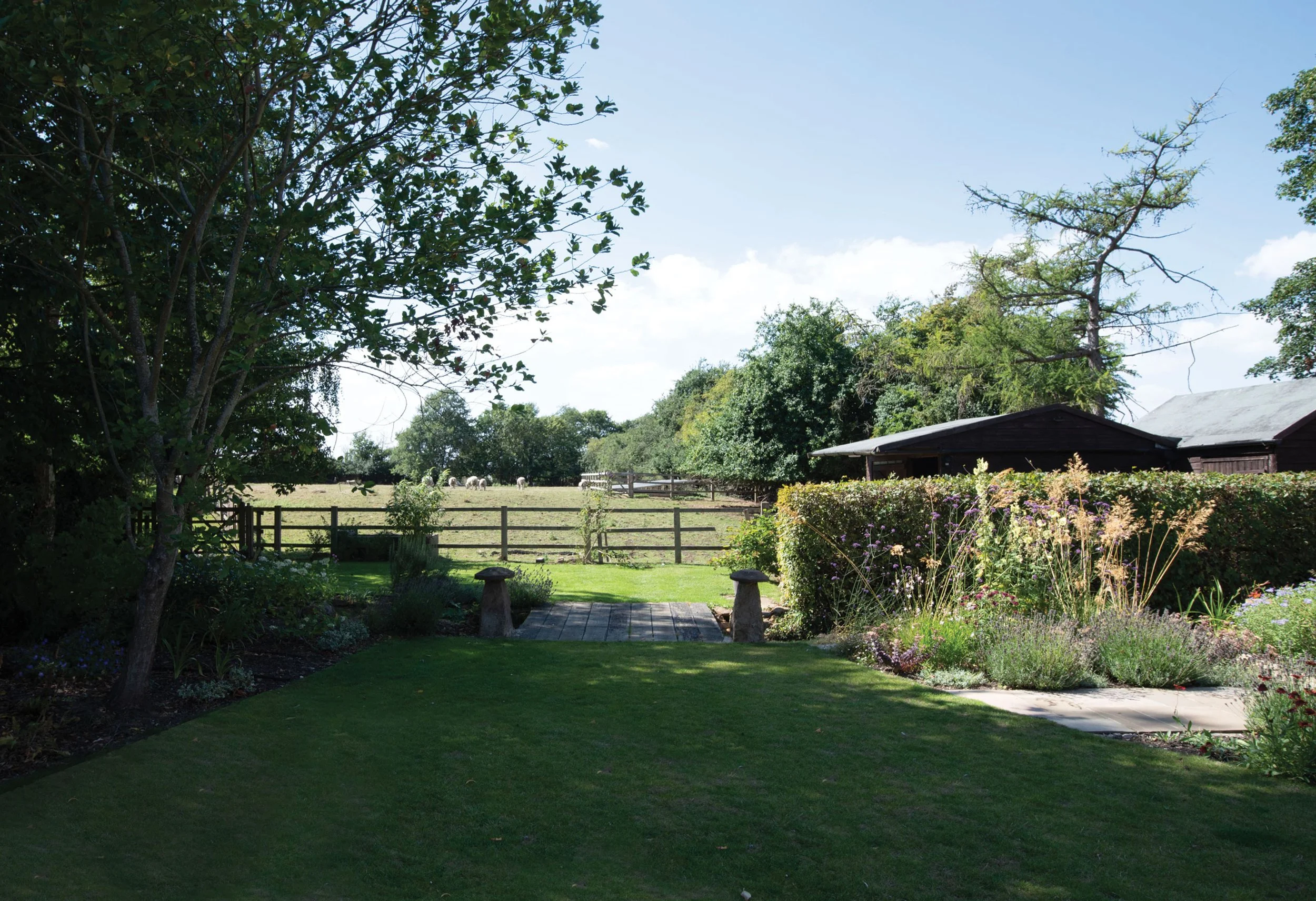 Lawn opening towards the surrounding rural landscape, with planted borders and mature trees framing views beyond the garden.