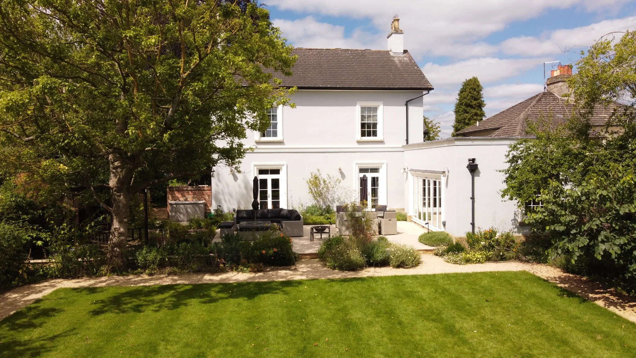 Georgian house overlooking a landscaped garden with mature trees, lawn and contemporary paving.