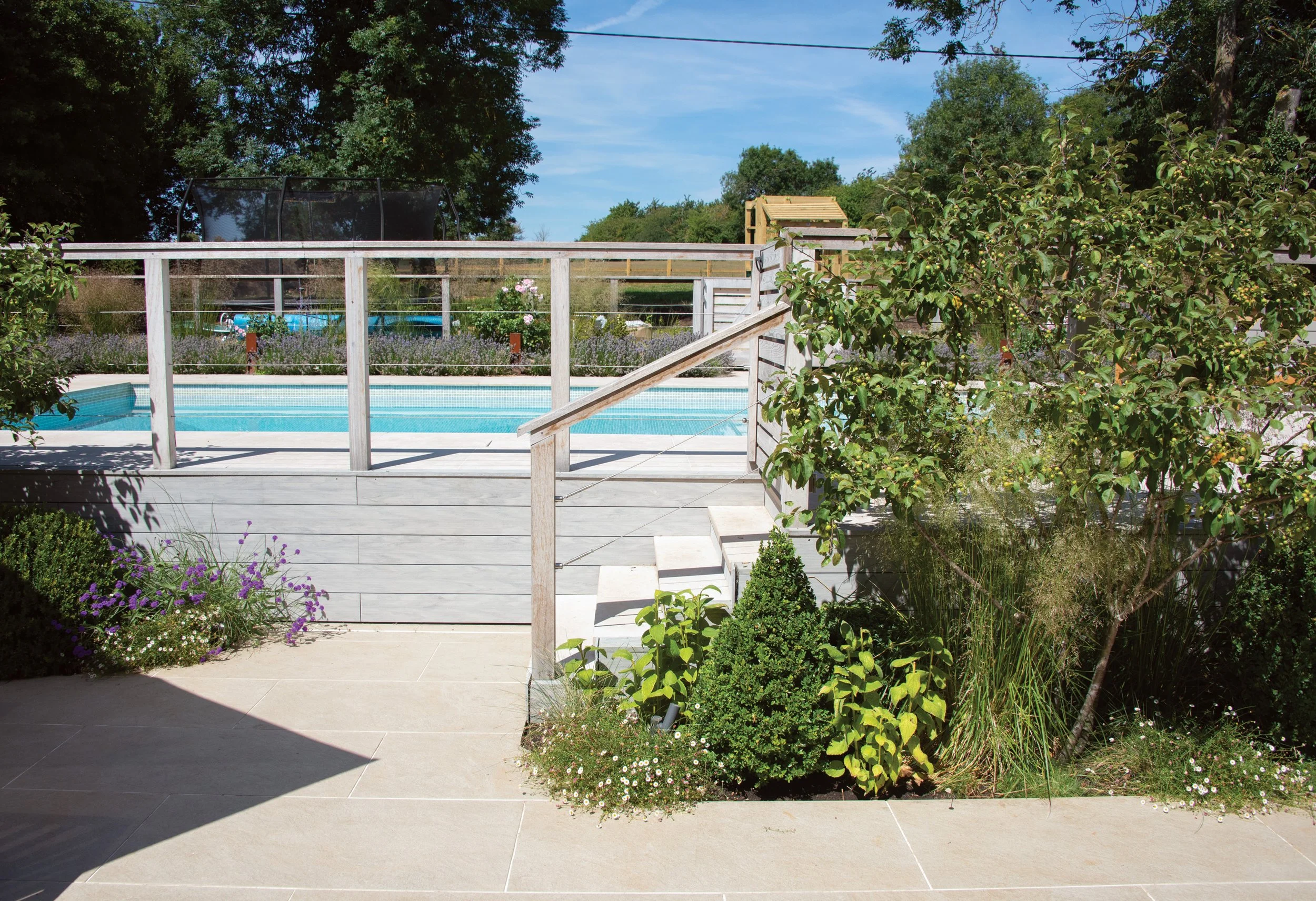 Completed pool garden with new retaining walls, timber balustrade, pale paving and integrated planting.