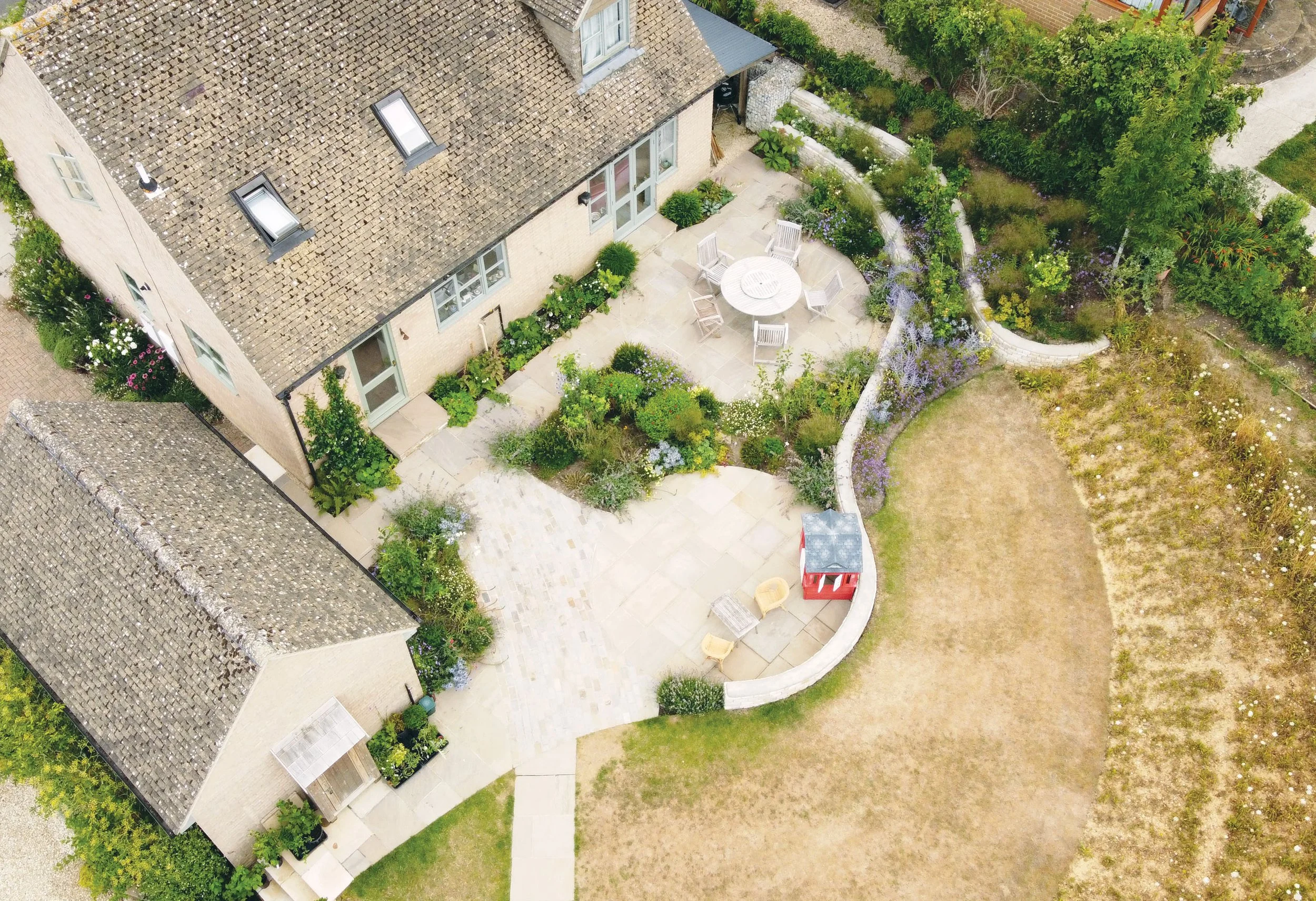 Aerial view of the redesigned garden beside the house, with two circular stone terraces and curving walls creating distinct family spaces.