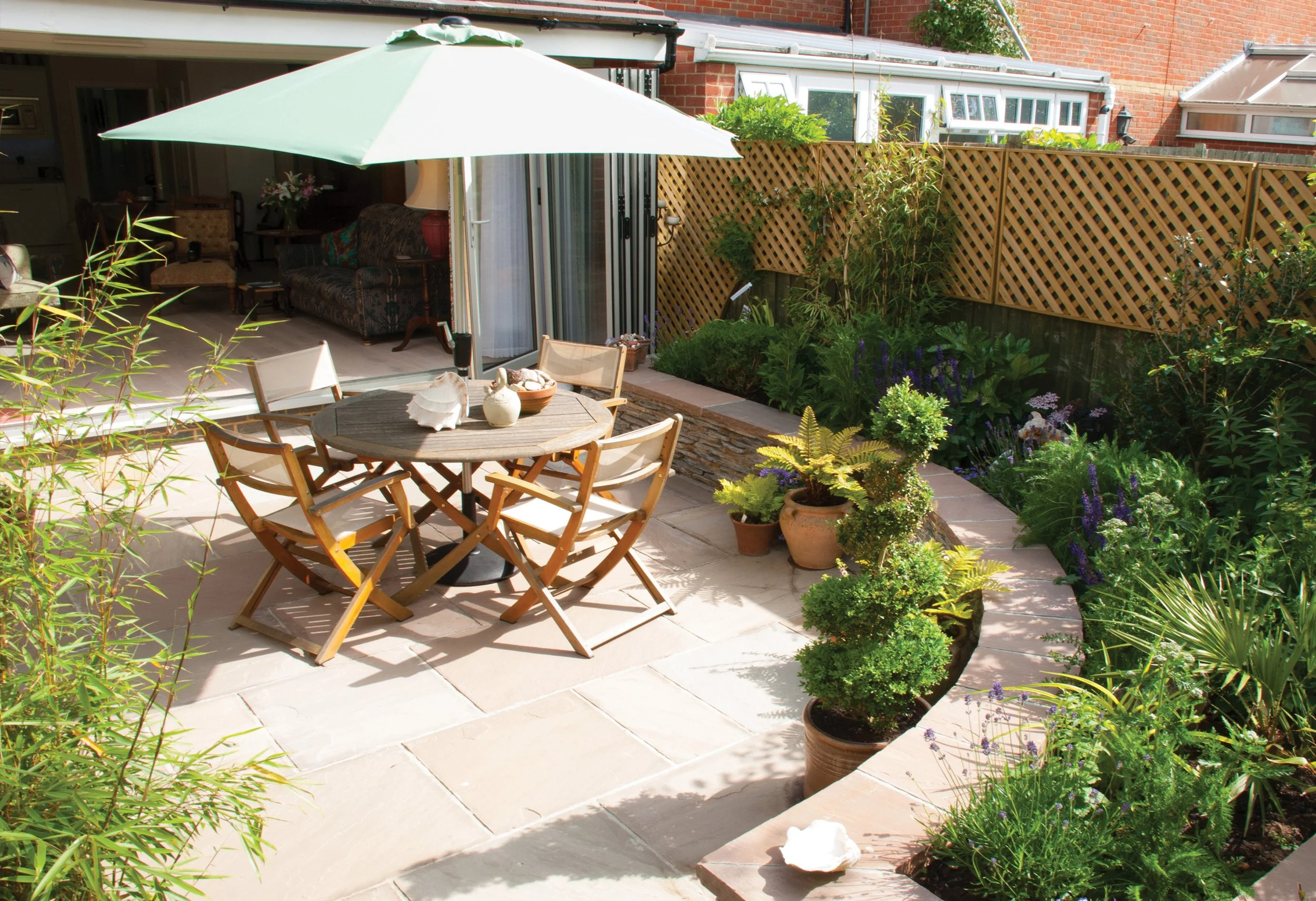 Small paved courtyard with outdoor dining, pots and layered planting creating an enclosed garden around the house.