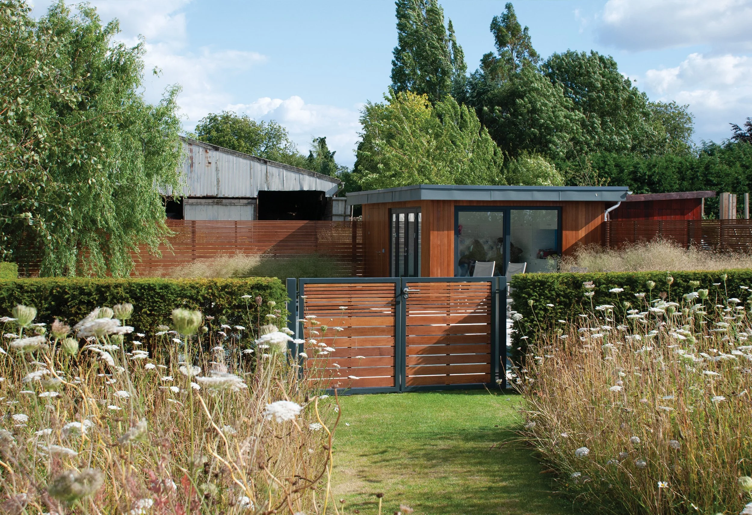 Bespoke cedar pool house and gates set against the looser wildflower planting beyond.