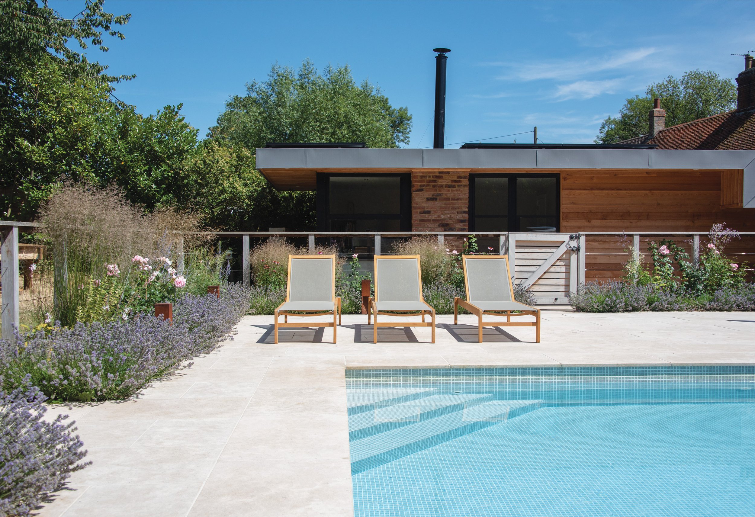 Contemporary garden building and poolside loungers surrounded by relaxed perennial and ornamental grass planting.