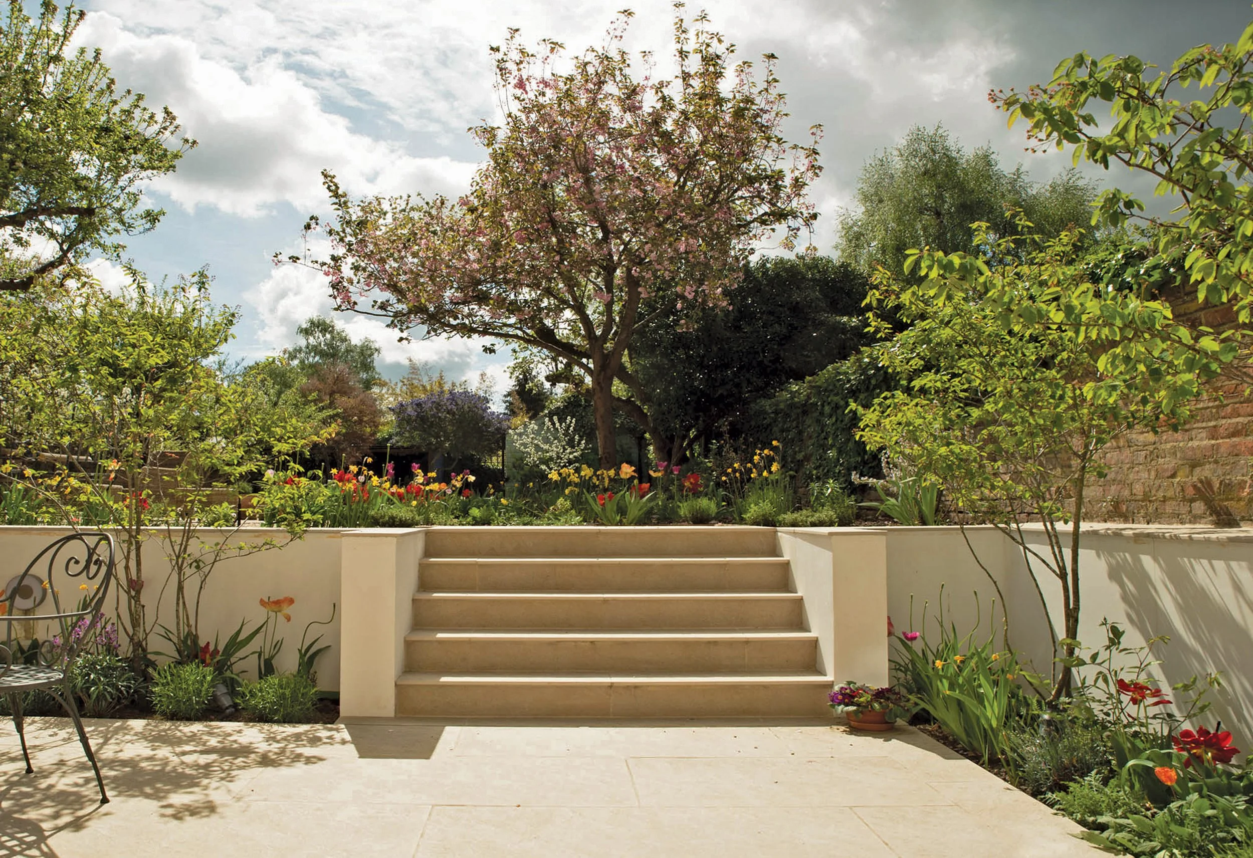 Formal stone steps framed by retaining walls and planting, leading towards a mature flowering tree.