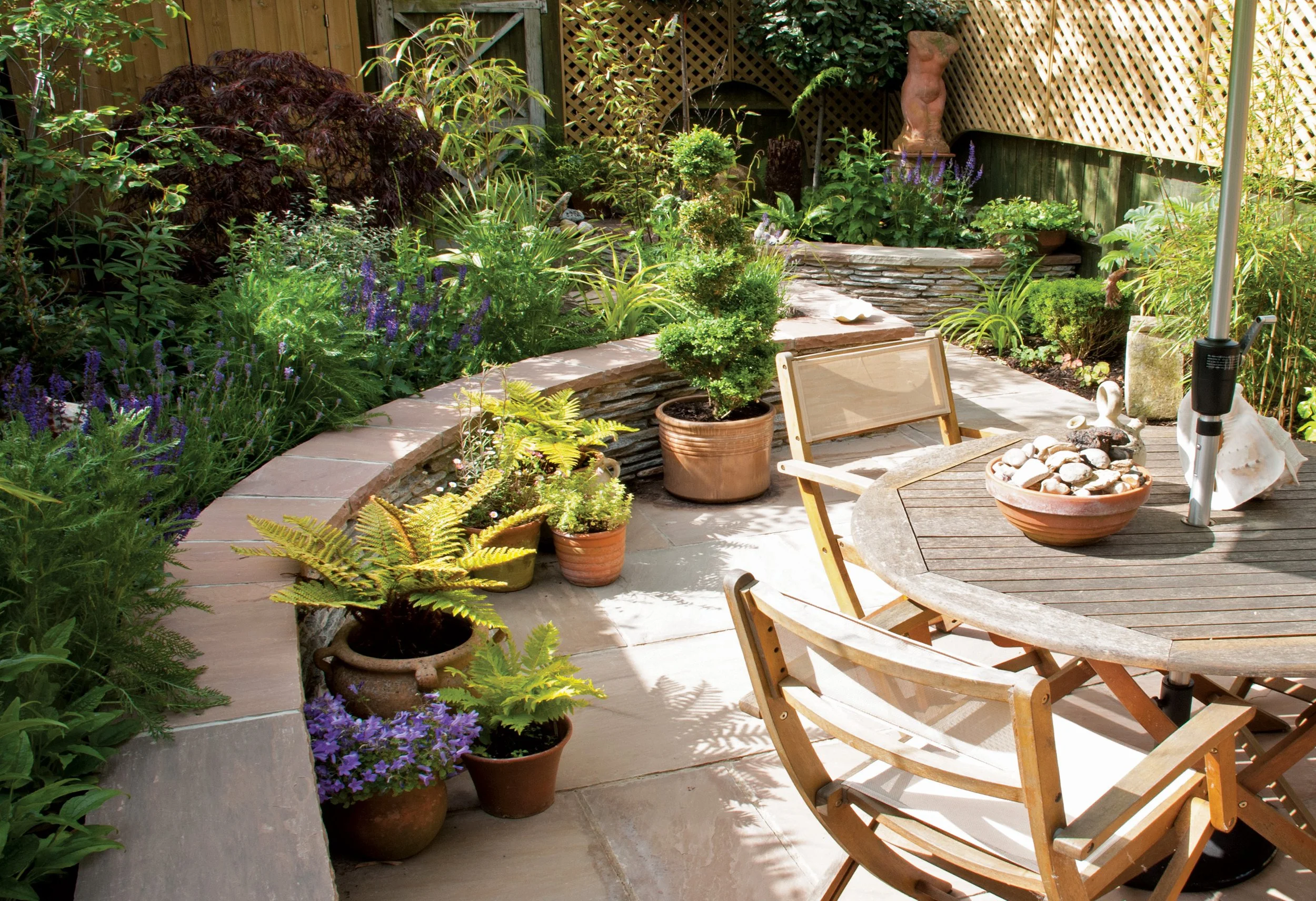 Intimate courtyard garden with curved paving, outdoor dining and abundant planting in beds and containers.