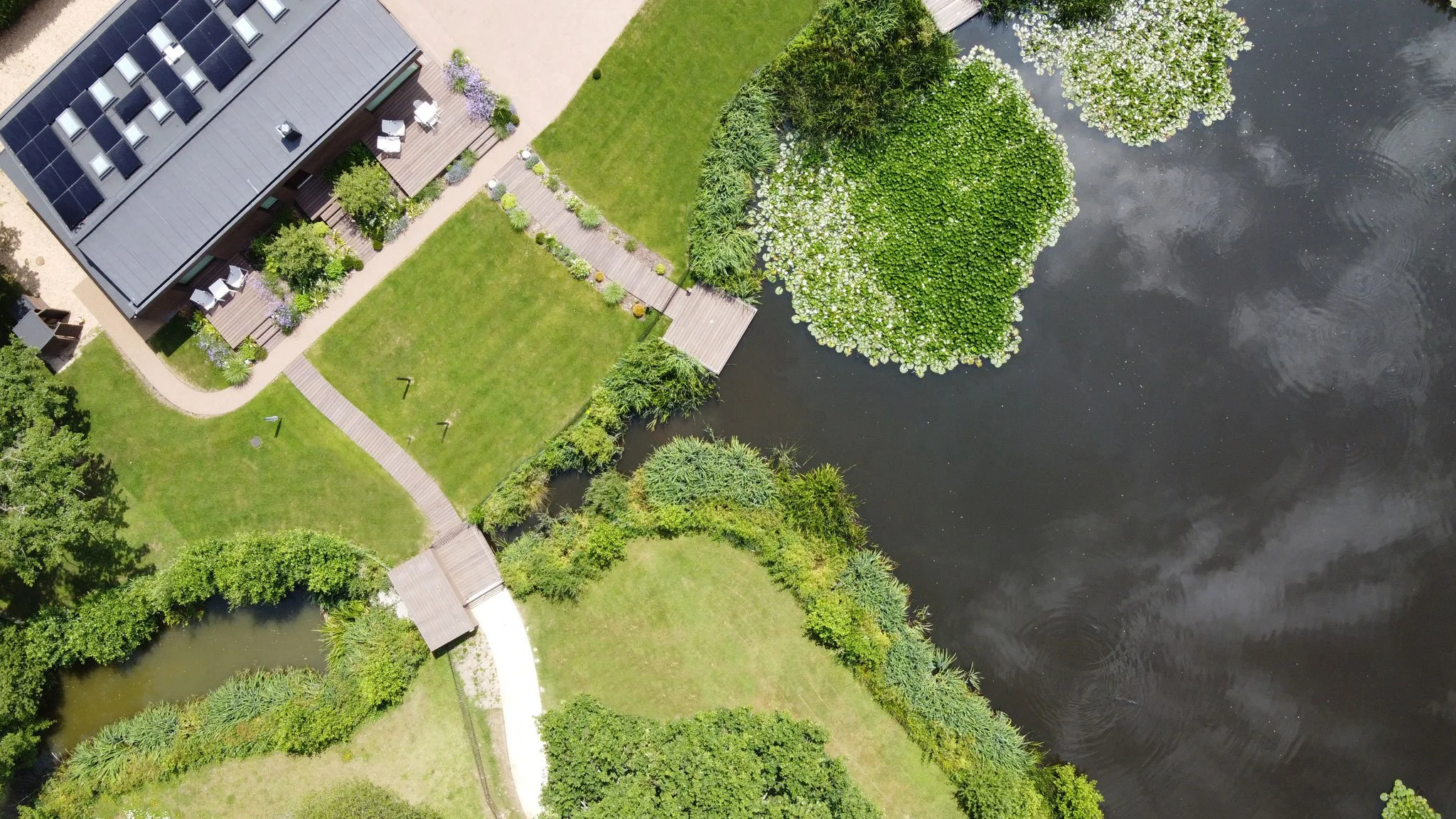 Overhead aerial of The Fishing Lodge showing the garden, timber decking, lawn and extensive water lilies on the fishing lake.