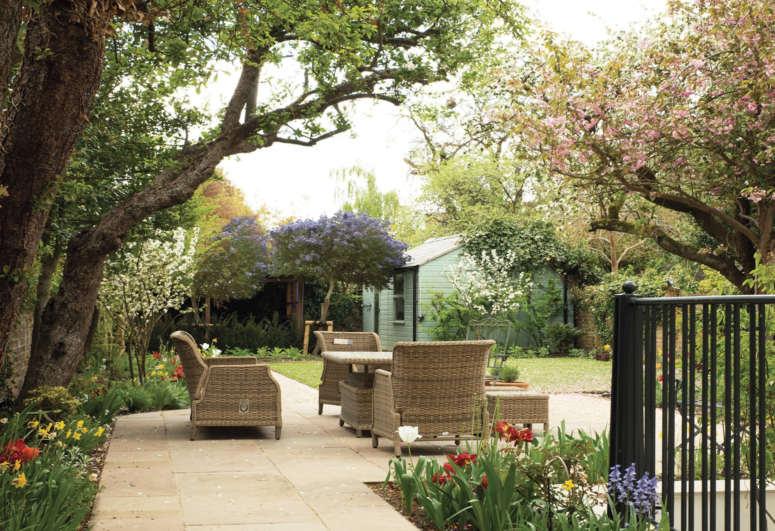 Secluded paved seating terrace beneath mature trees, surrounded by generous perennial planting.