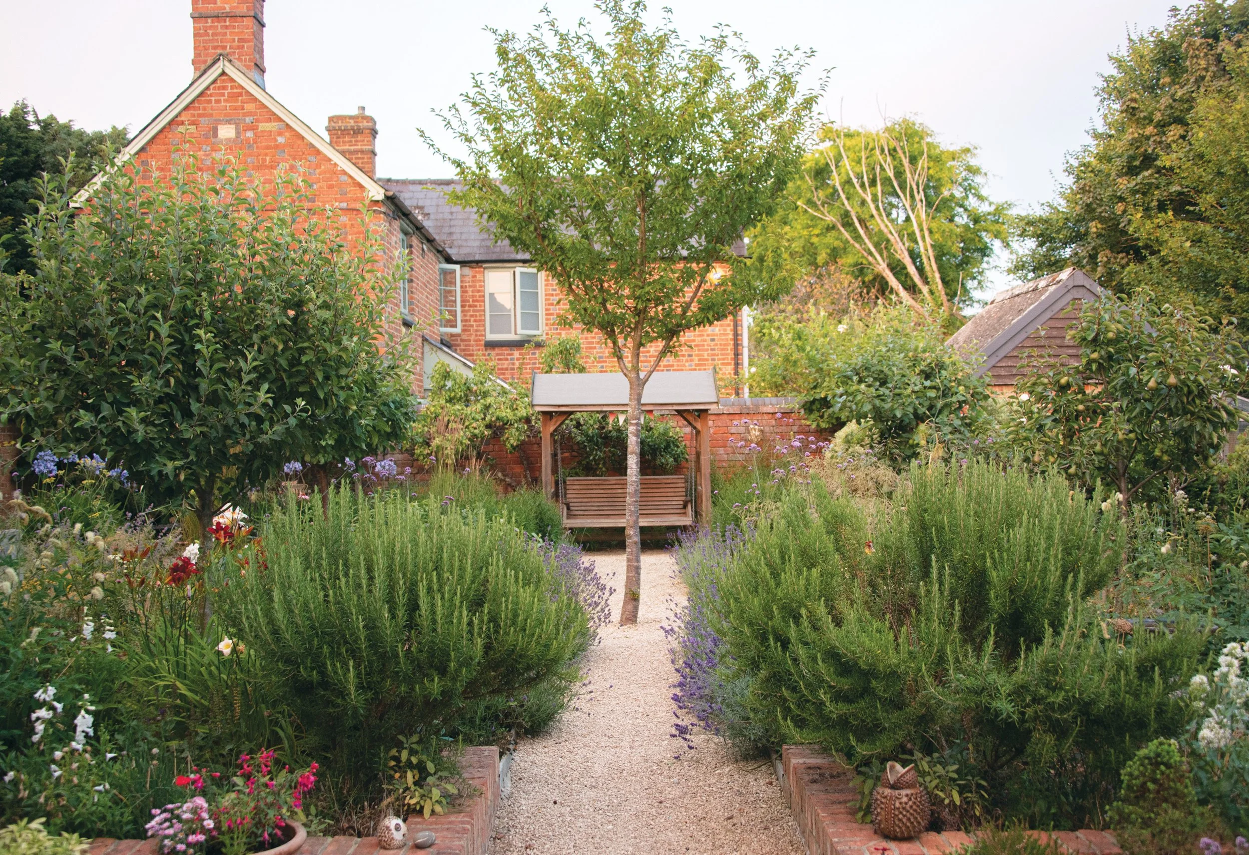 Formal view through the garden towards an arbour seat, framed by the central cherry tree and mixed perennial planting.