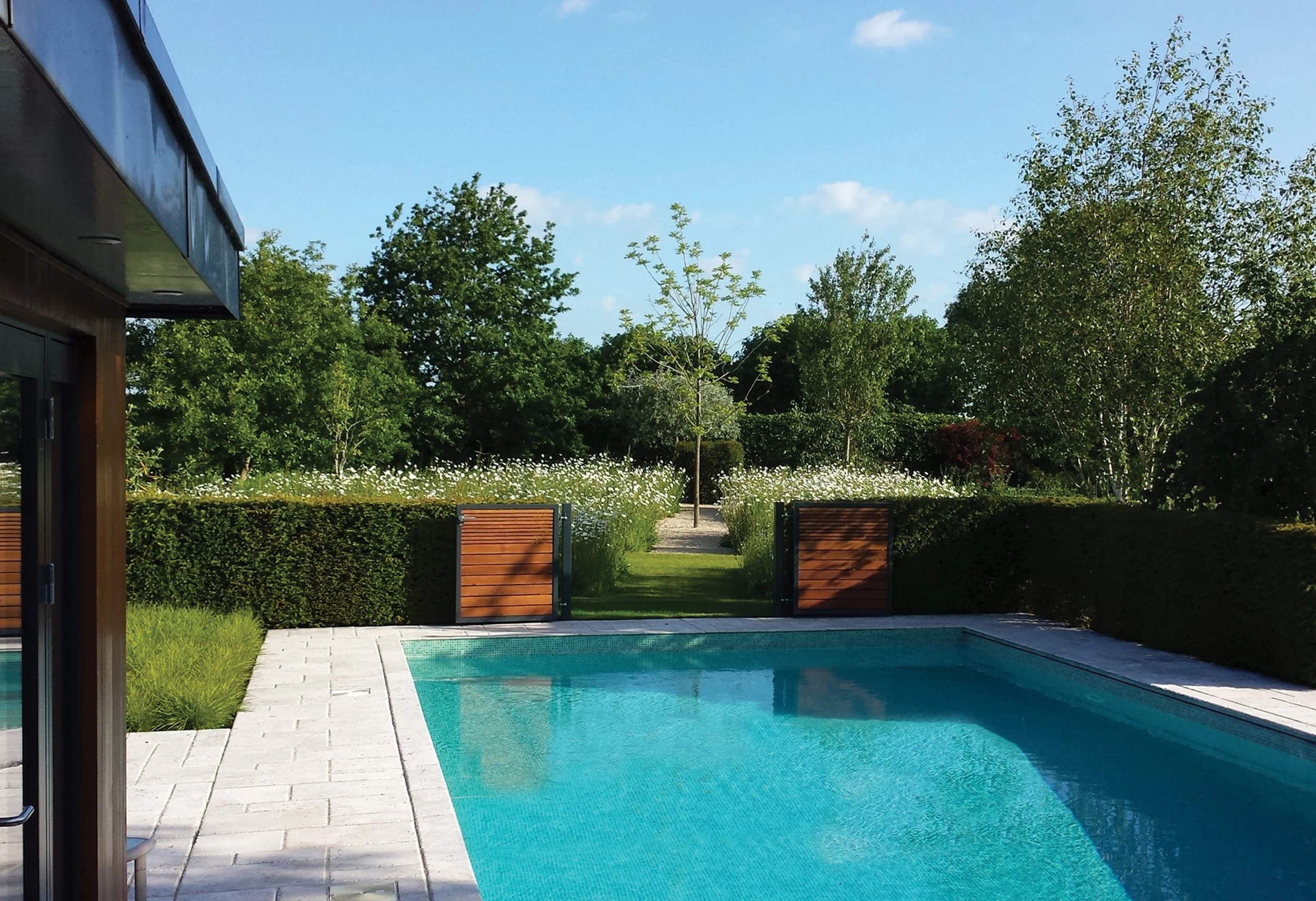 Swimming pool with the bespoke gates opened towards the wildflower meadow and mature walnut tree beyond.