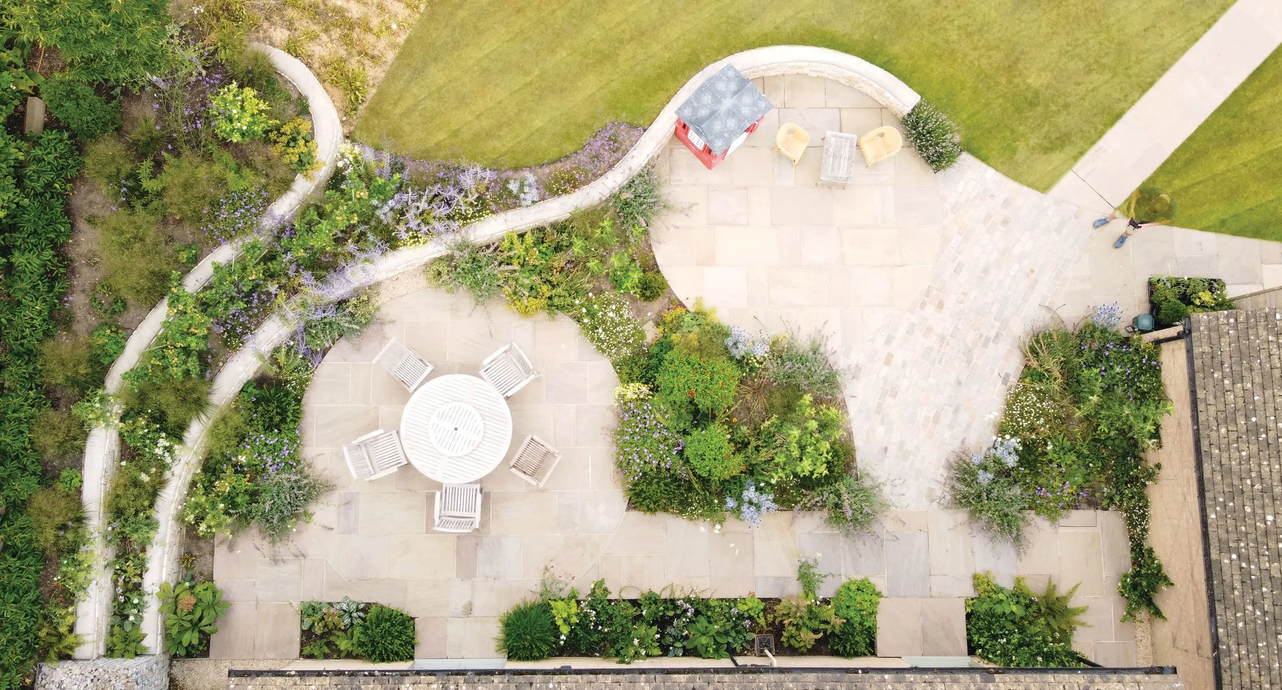 Overhead view of two circular stone terraces connected by curving walls and richly planted borders.
