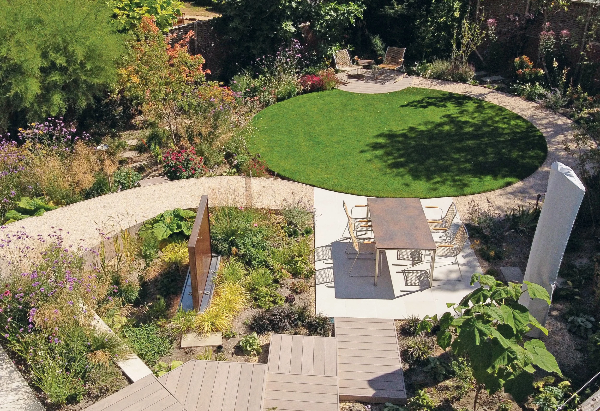 Aerial view of a small contemporary garden with circular lawn, curved paths, timber decking and densely planted borders.