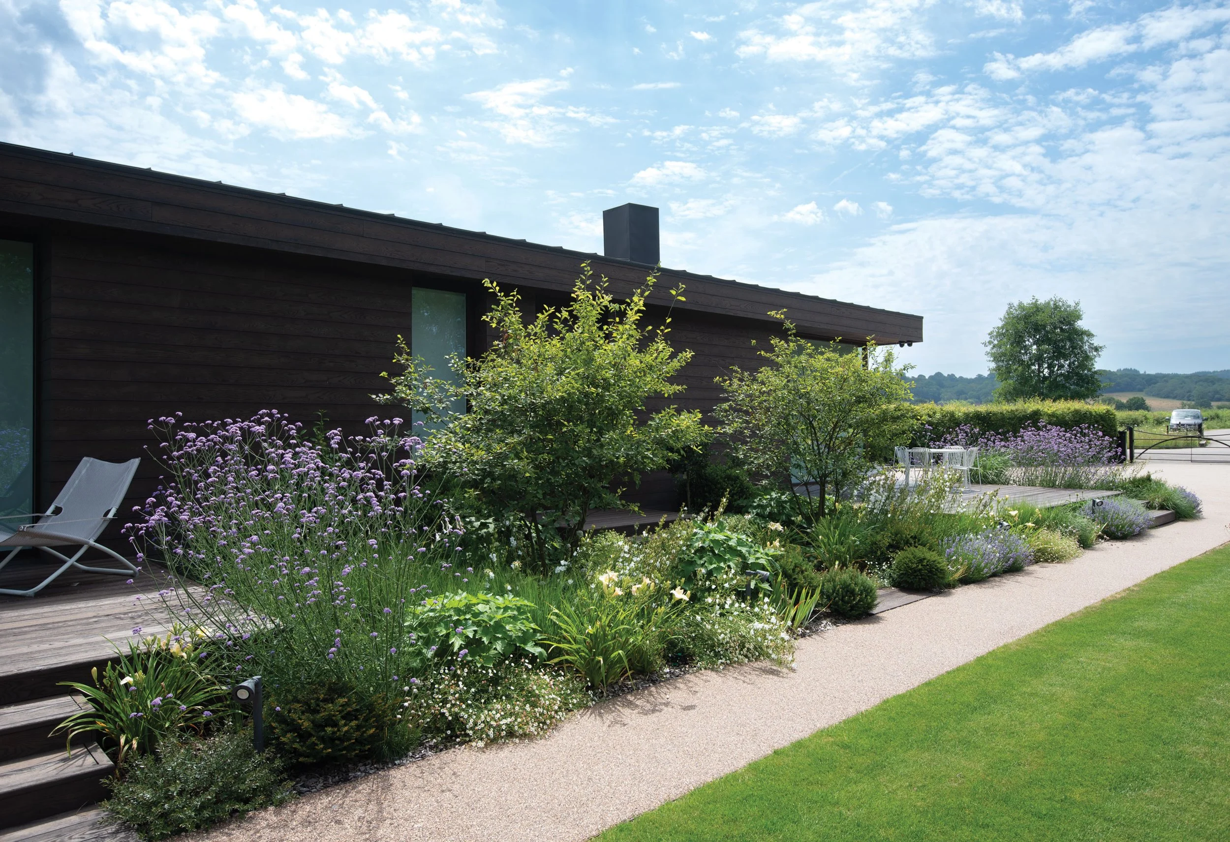 Long-flowering perennial planting and multi-stem Amelanchier trees beside the dark timber-clad Fishing Lodge.