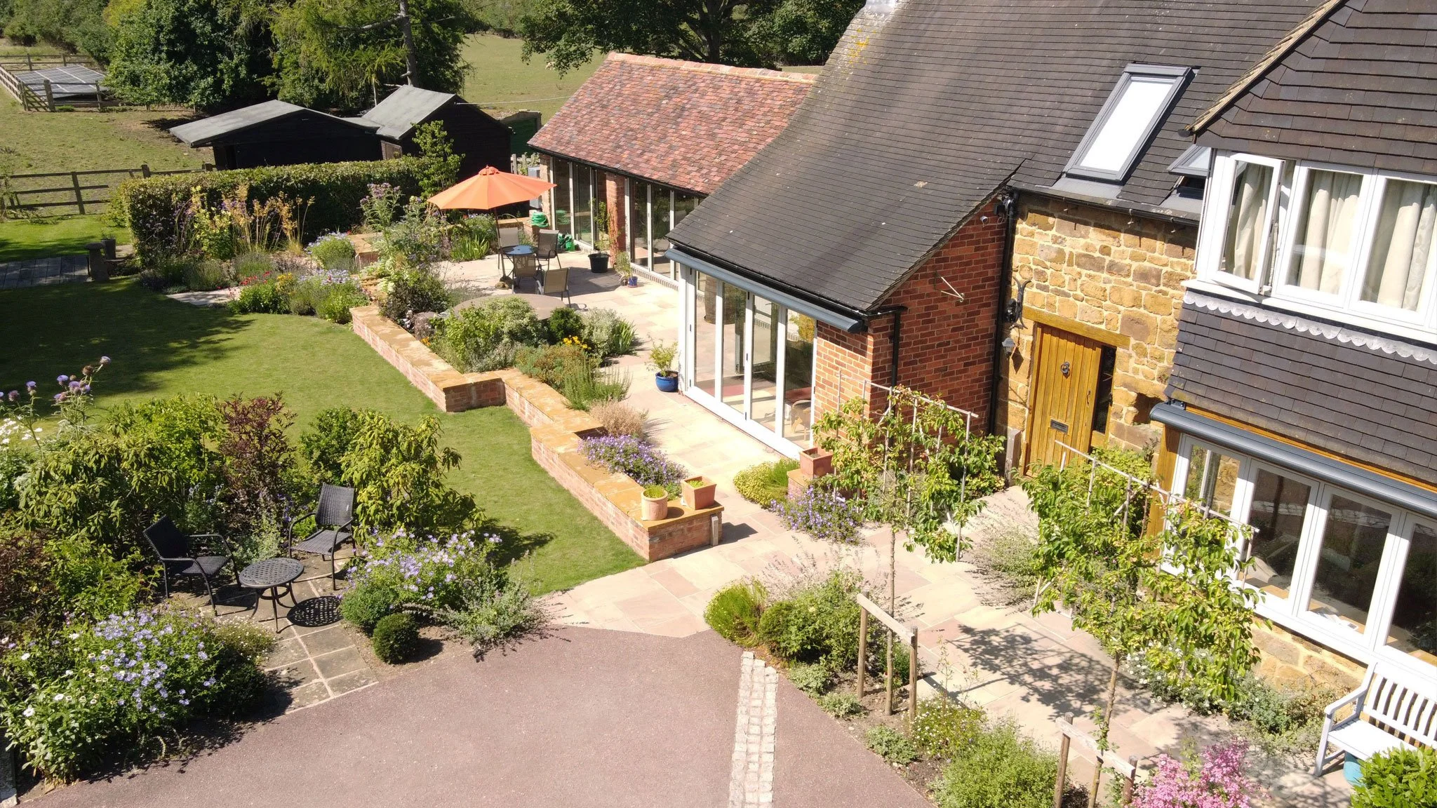 Converted barns and courtyard with perennial planting, low walls and paved routes forming the enclosed garden.