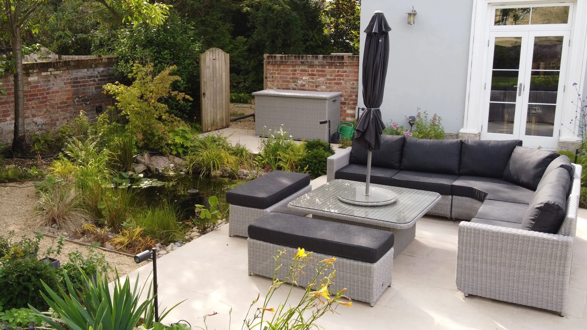 Contemporary outdoor seating beside a small garden pond, surrounded by naturalistic planting.
