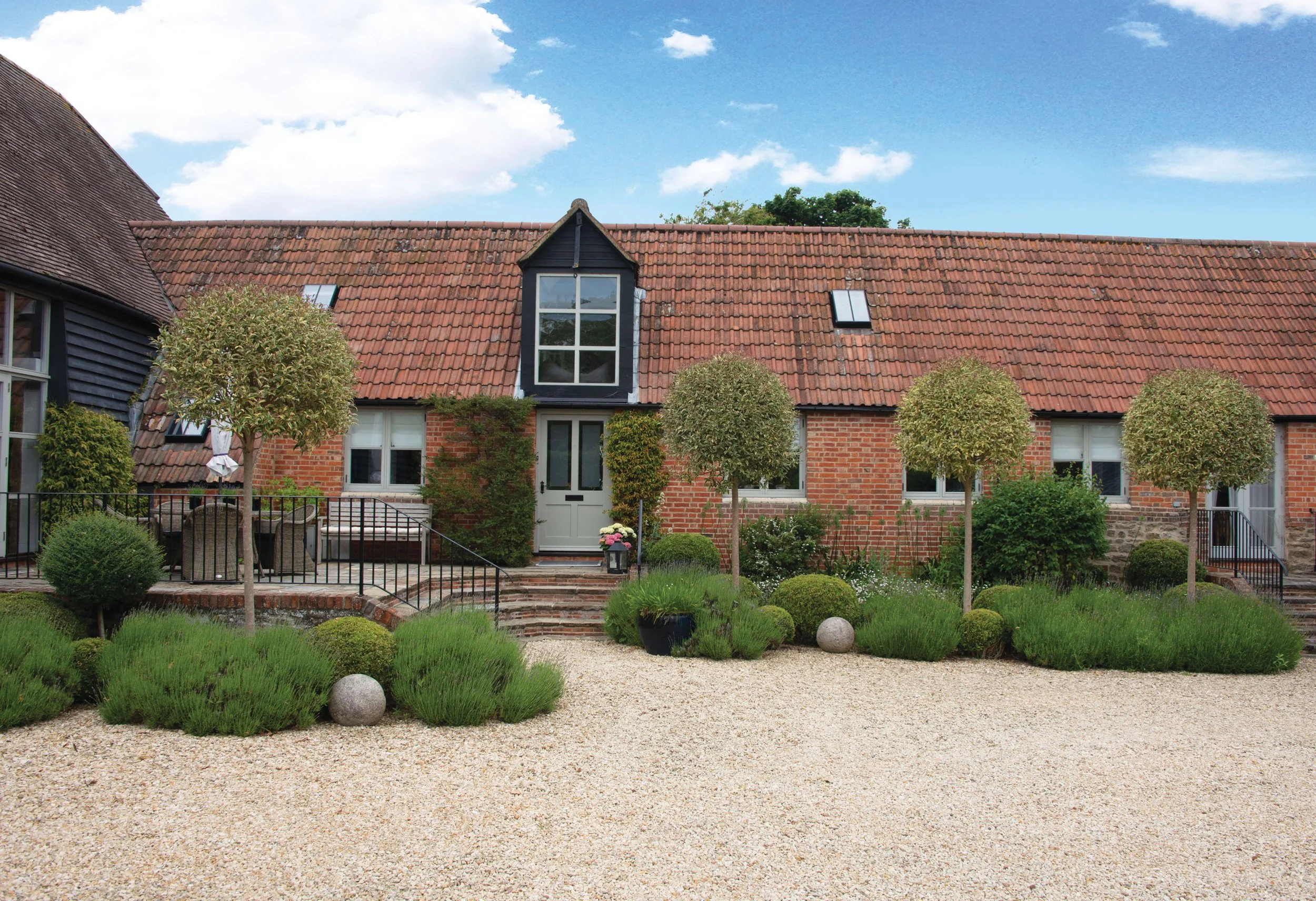 Formal courtyard planting with repeating Ligustrum × excelsum ‘Superbum’ trees and lavender softening the gravel entrance to the barn.
