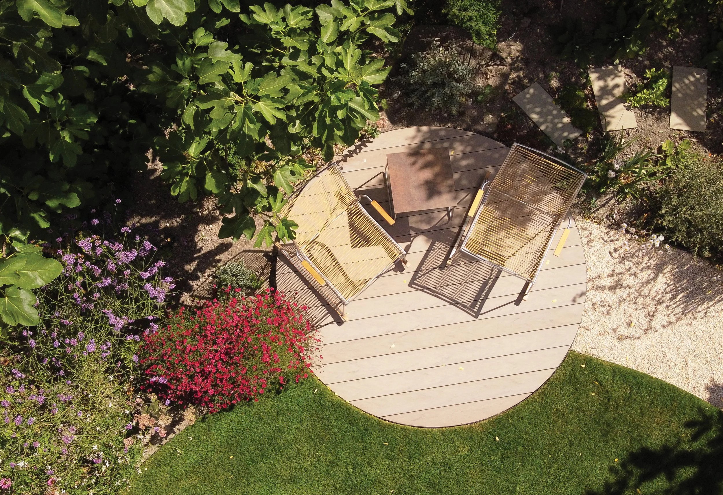 Circular composite decking seating terrace tucked into a small garden and surrounded by colourful planting.