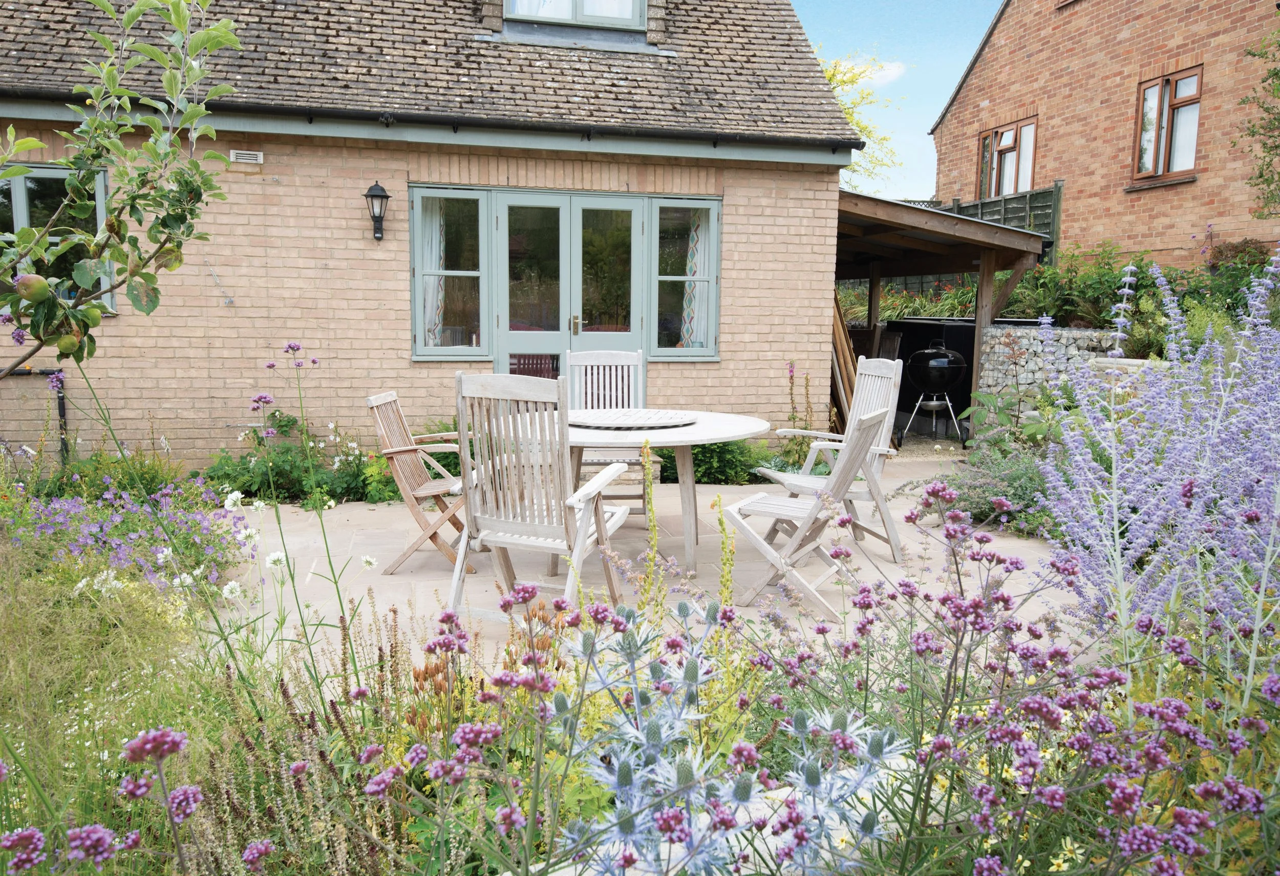 Garden terrace surrounded by loose flowering planting, with the stone house forming the backdrop.