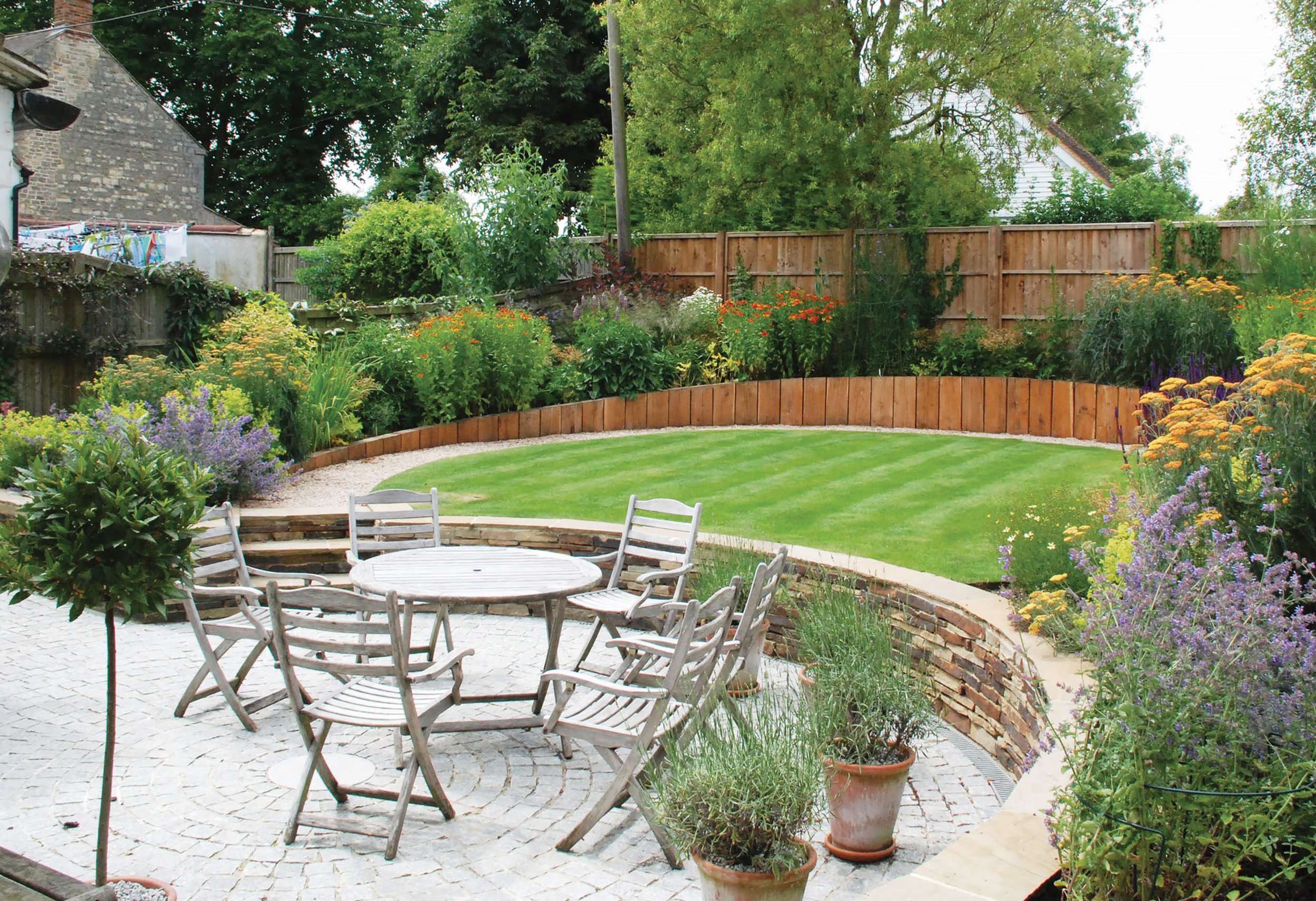 Curved family garden with circular lawn, timber retaining walls, perennial planting and outdoor dining terrace.