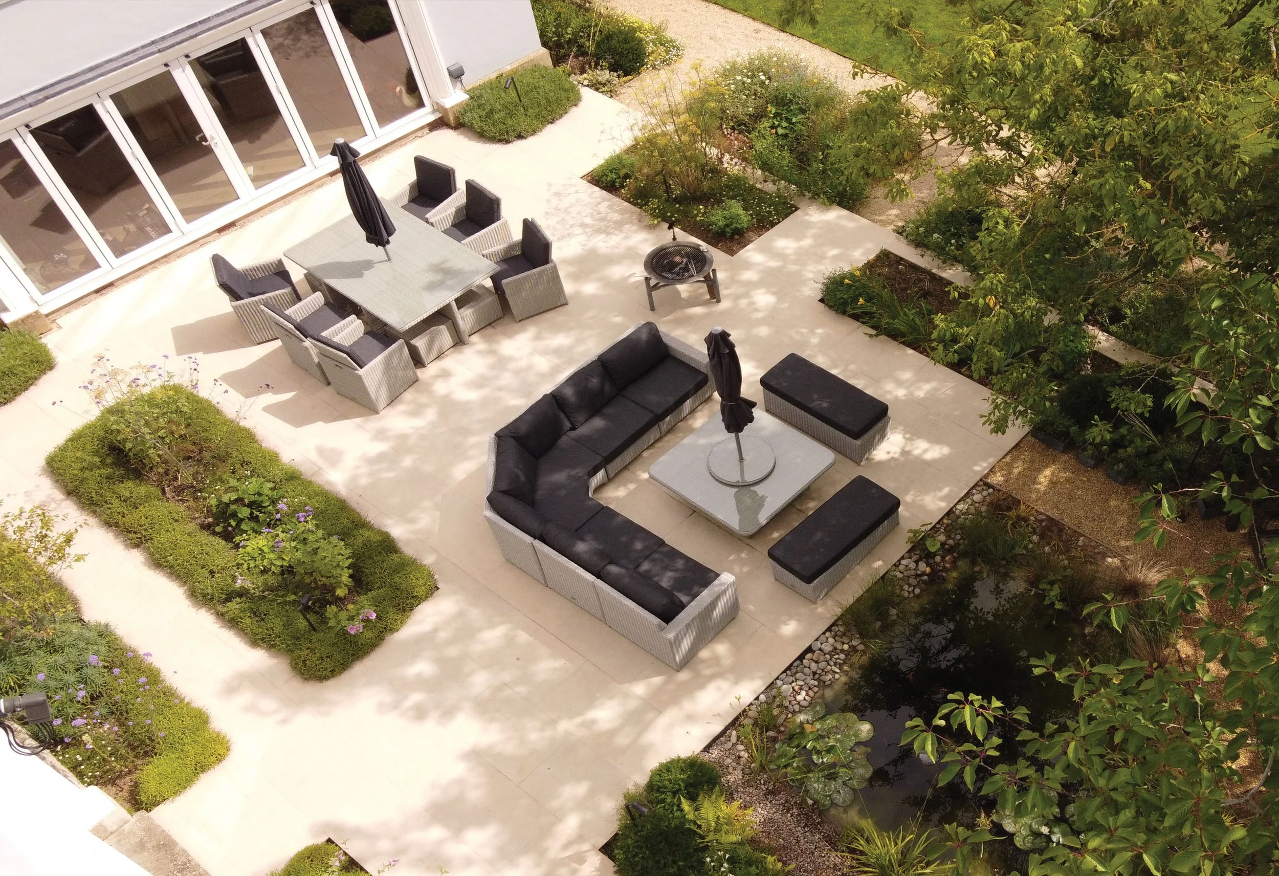 Contemporary paved terrace with outdoor seating surrounded by formal planted beds and mature trees.