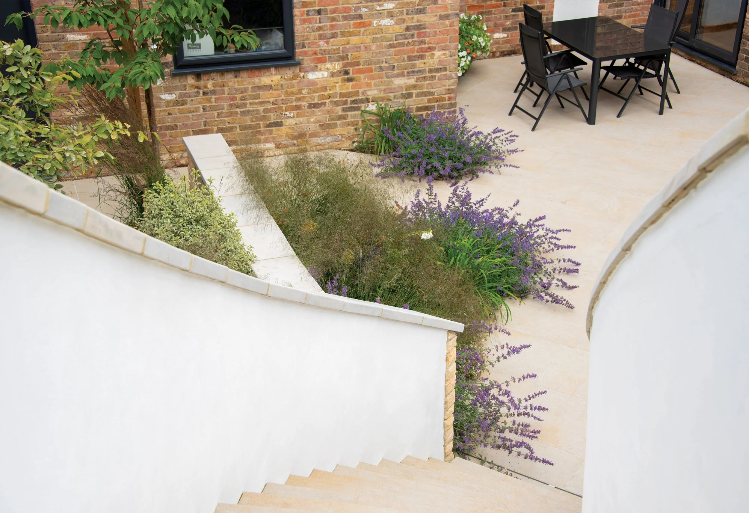 Lower terrace and planting beside the house, with curved walls and steps connecting to the garden above.